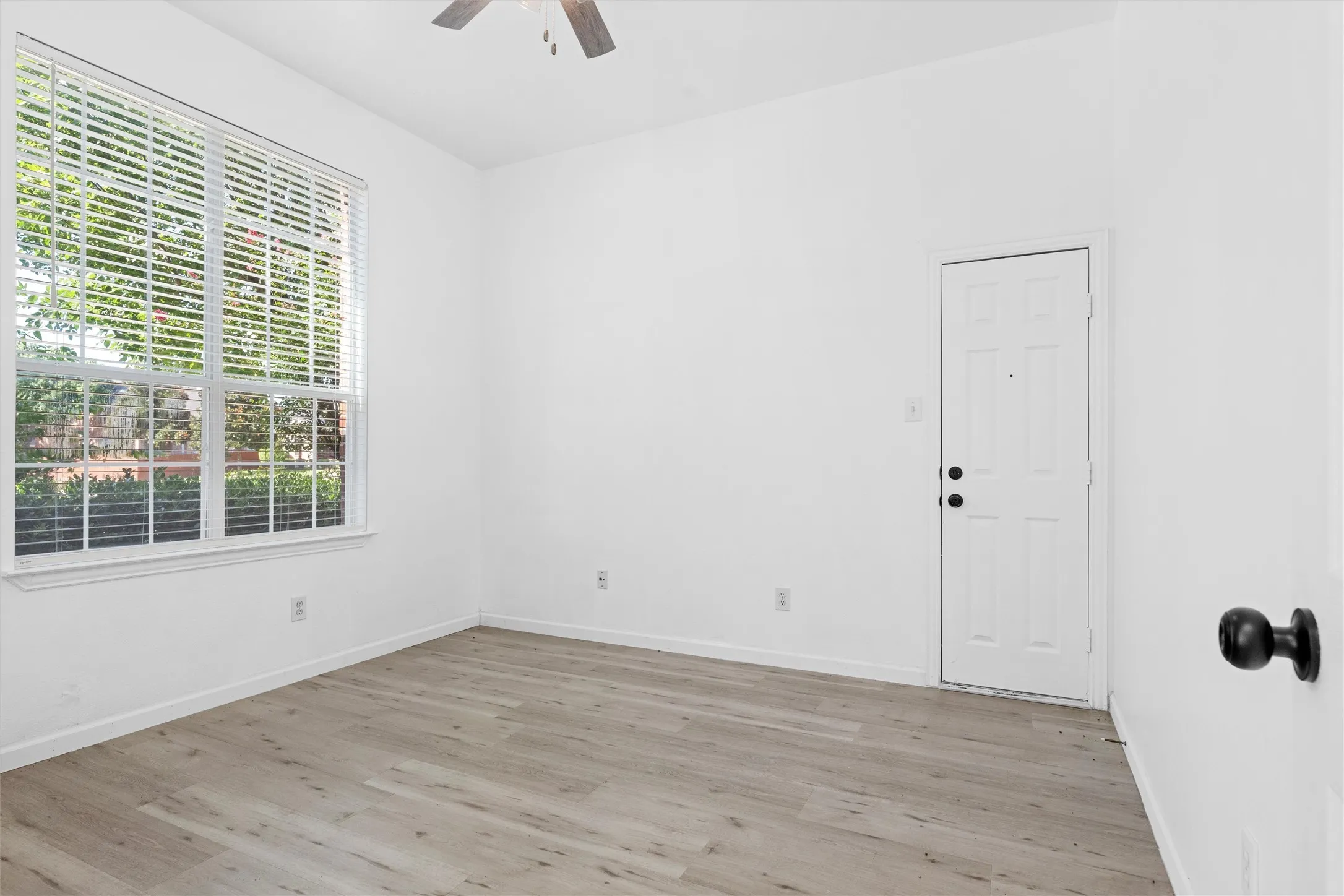 Wood-finish flooring, white walls, and a large window with blinds