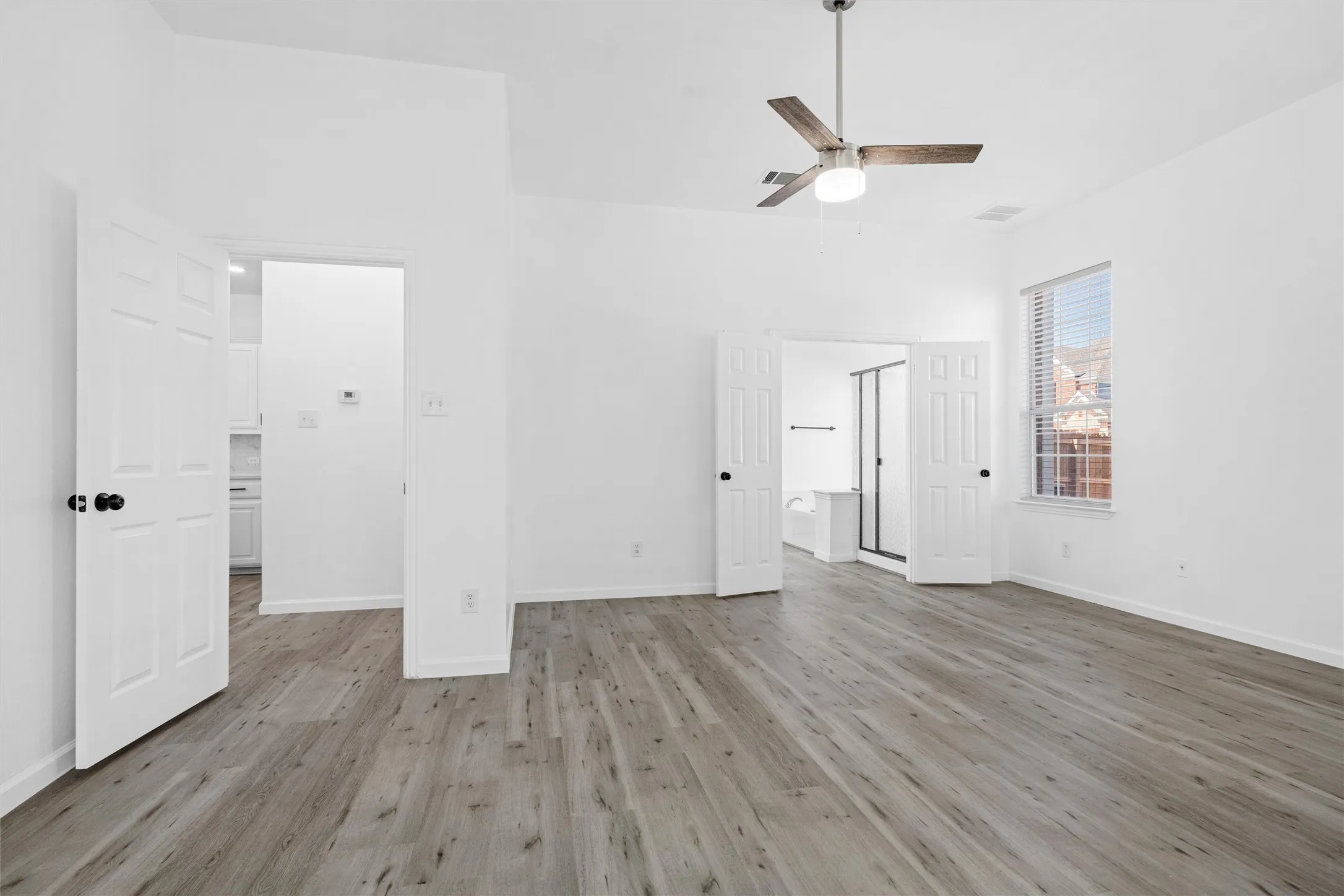 Wood-finish flooring, ceiling fan with integrated lighting, white paneled doors, and a window with blinds