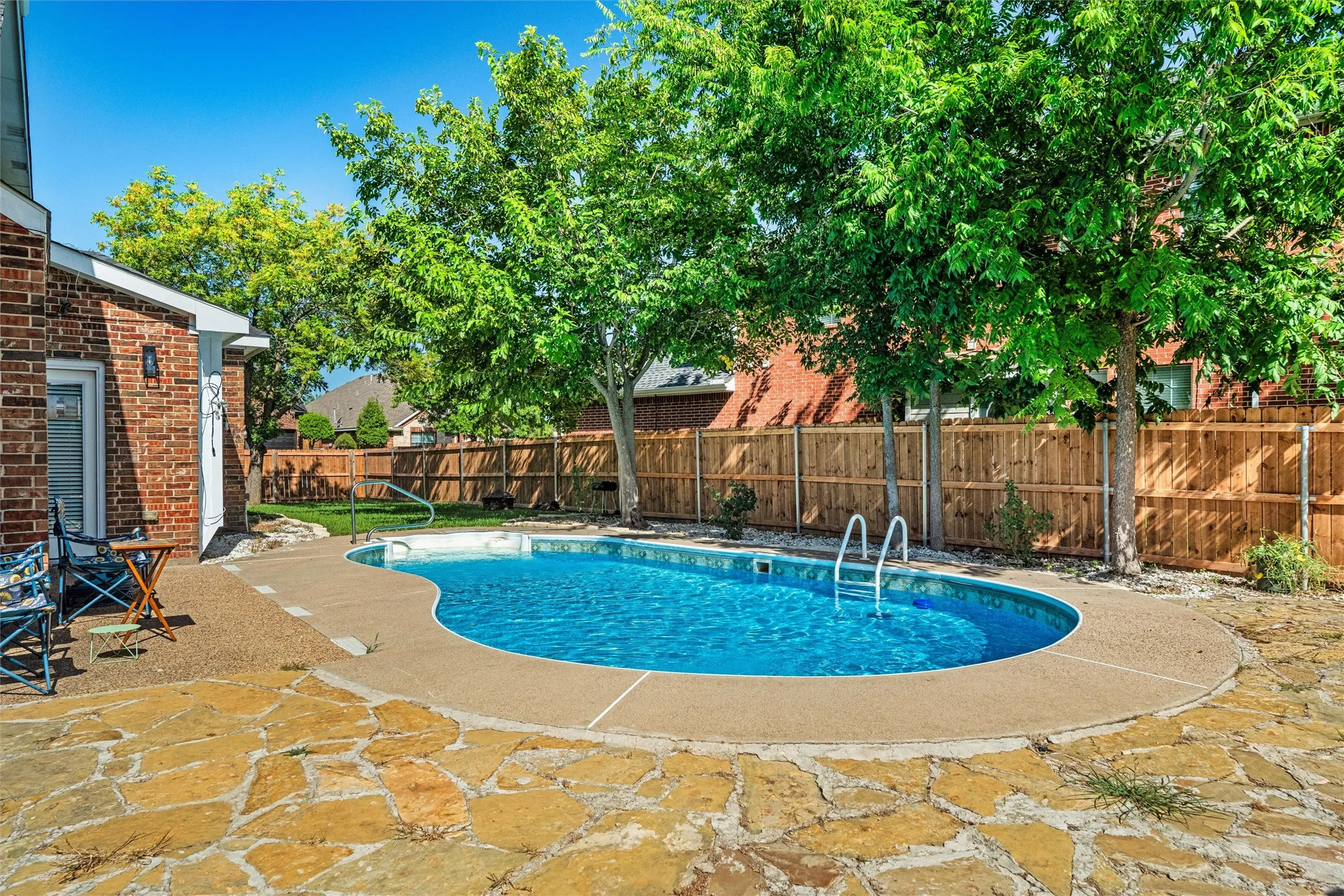 Fenced backyard featuring a freeform swimming pool with integrated steps, flagstone patio, and mature trees