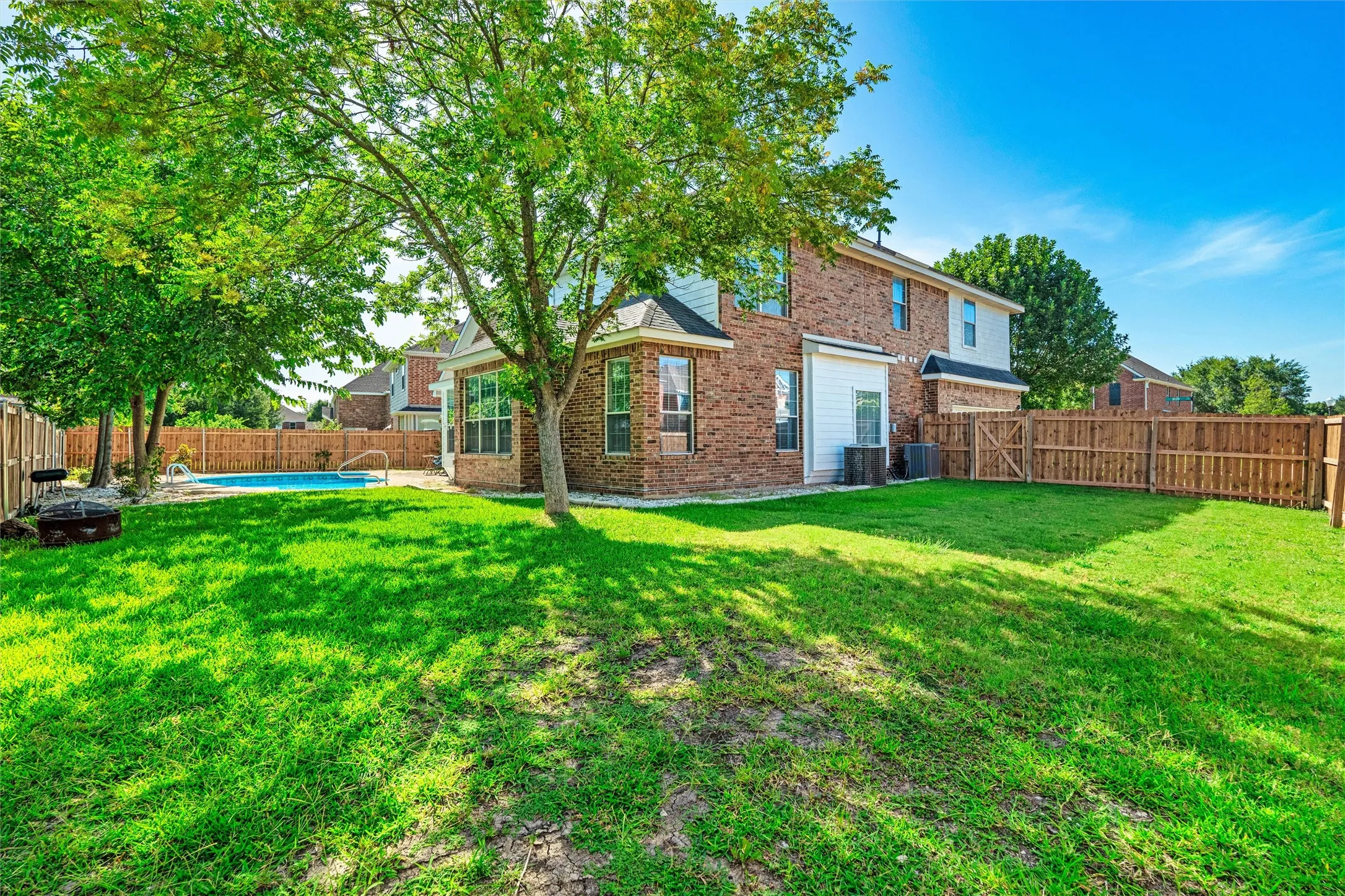 Expansive backyard featuring a swimming pool, mature trees, and a wooden privacy fence