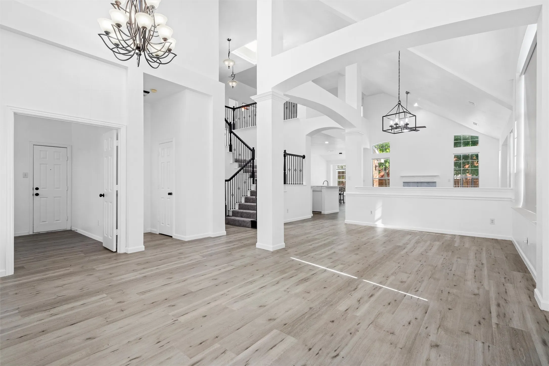Vaulted ceilings with exposed beams, wood-finish flooring, two-story foyer, iron-railed staircase, and decorative chandeliers