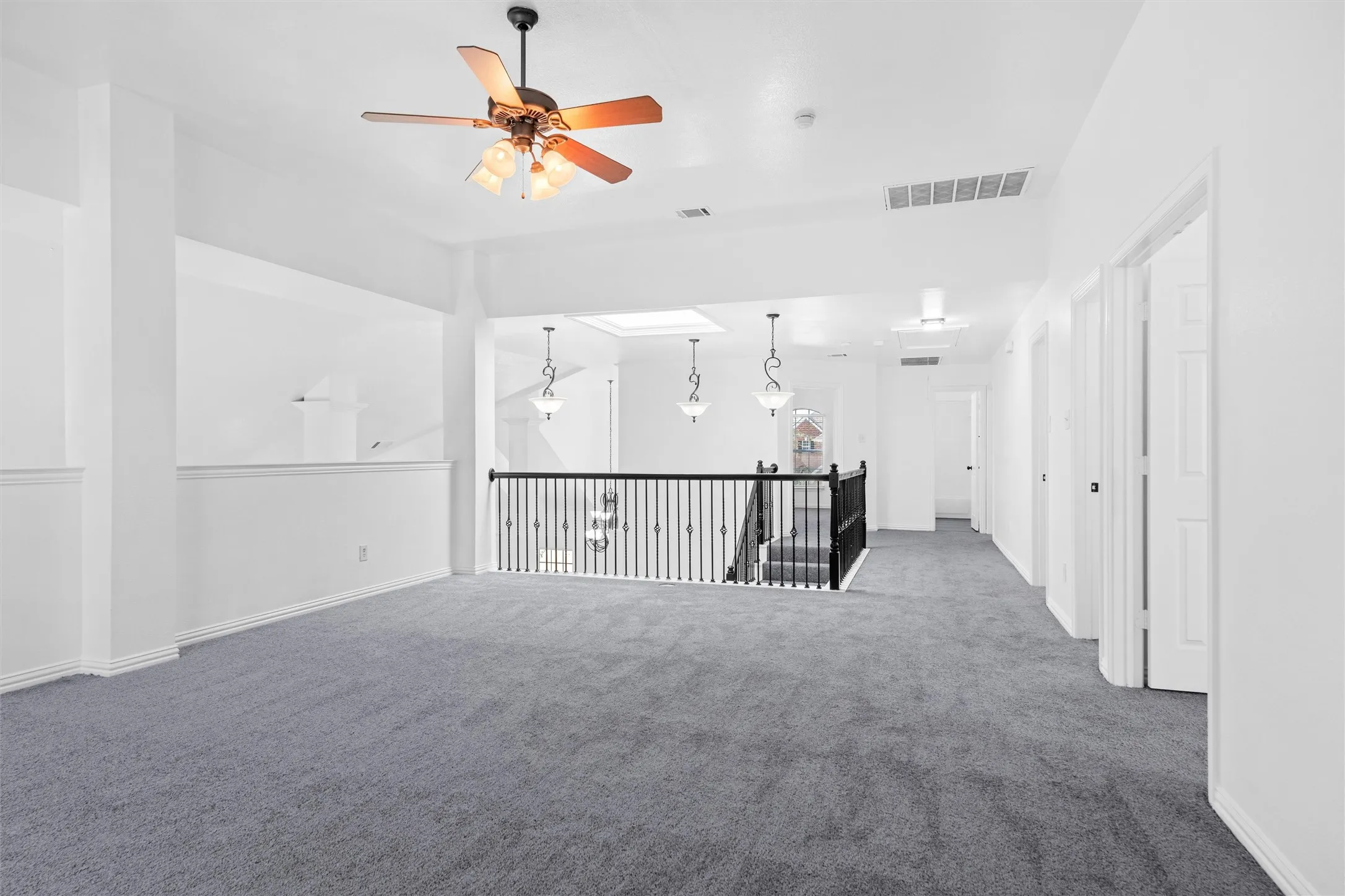 Spacious carpeted area with a ceiling fan, a skylight, and a staircase with a black metal railing