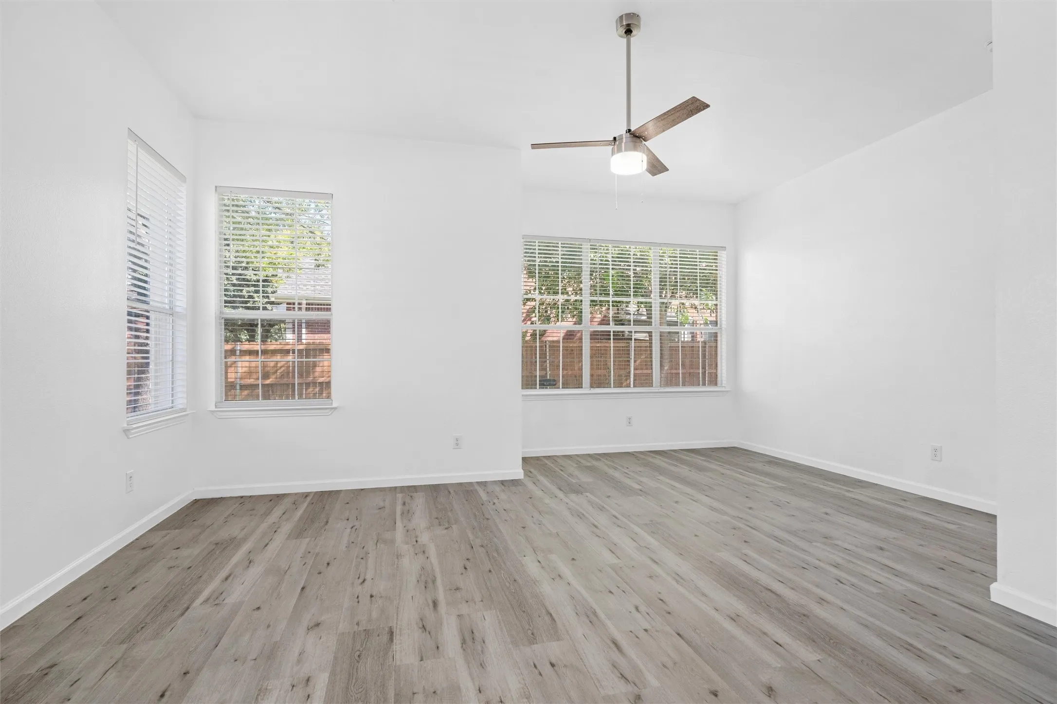 Spacious room with wood-finish flooring, multiple windows, and a ceiling fan