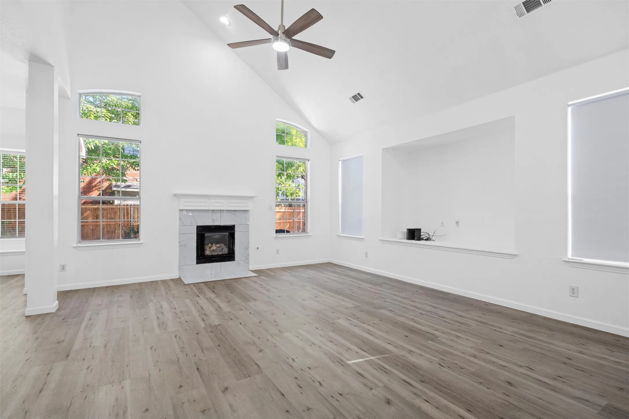 Vaulted ceiling, wood-finish flooring, tiled fireplace with mantel, recessed wall niche, and ceiling fan