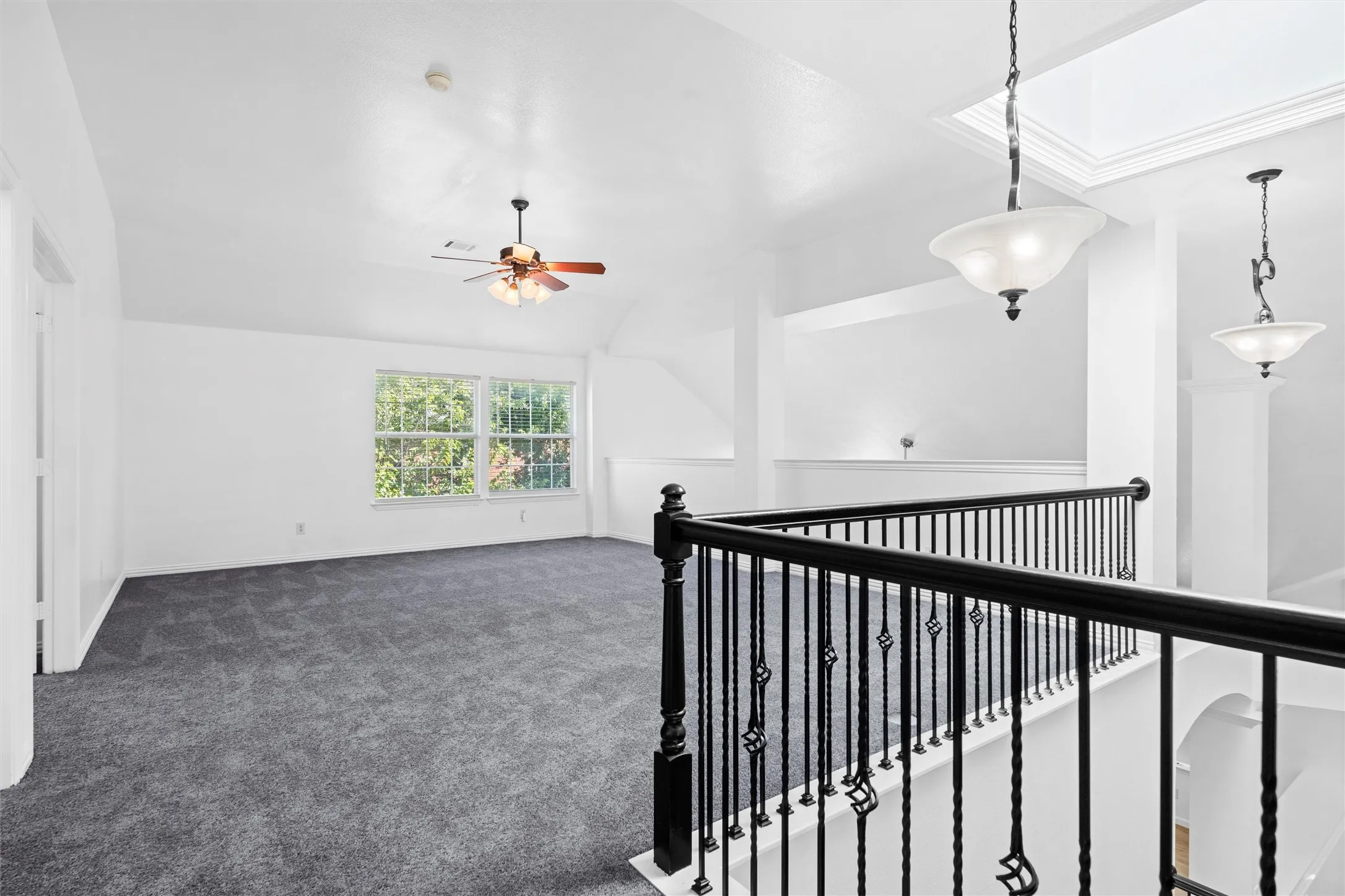Vaulted ceiling with ceiling fan, dual windows, gray carpeting, and black iron balusters