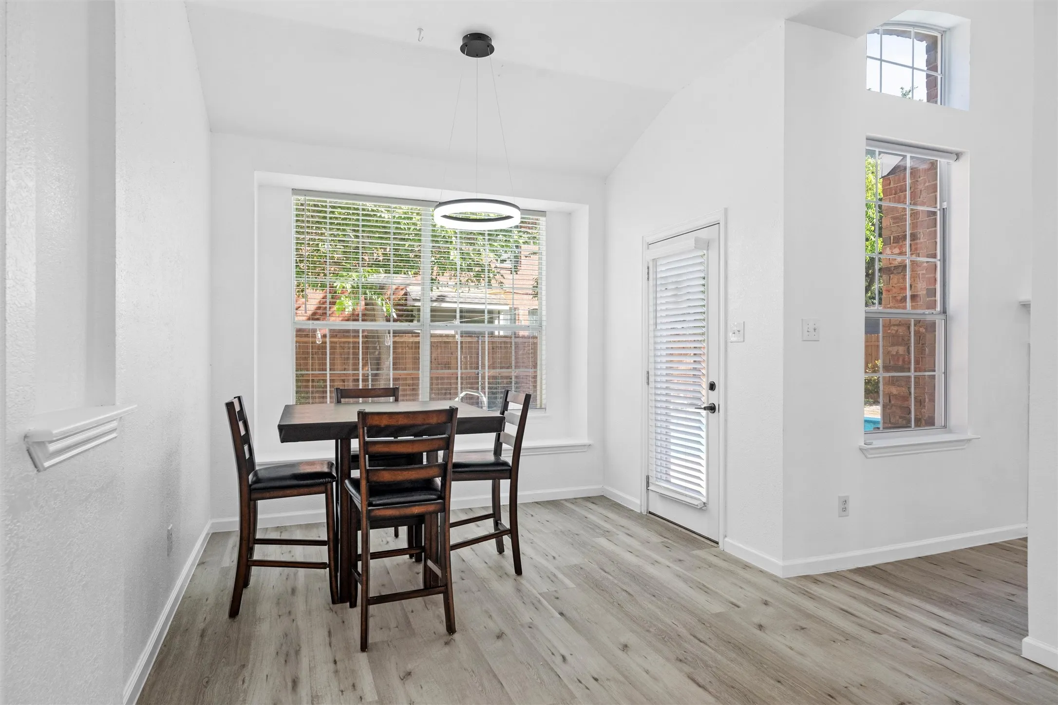 Wood-finish flooring, vaulted ceiling, contemporary pendant light fixture, large windows, and a glass-paned exterior door