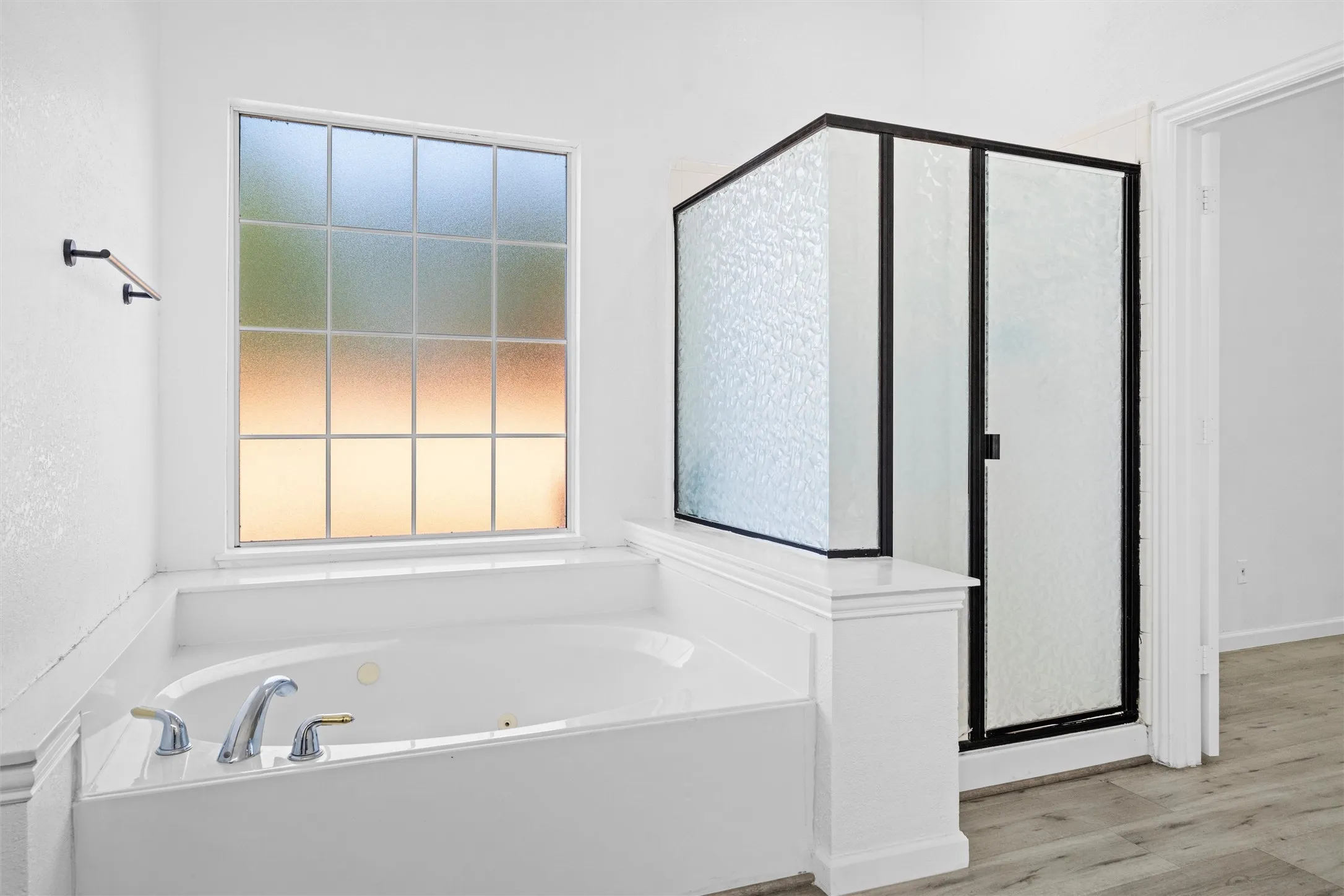 Soaking tub with deck-mounted chrome fixtures, frosted privacy window, and an adjacent shower enclosure with black framing and textured glass
