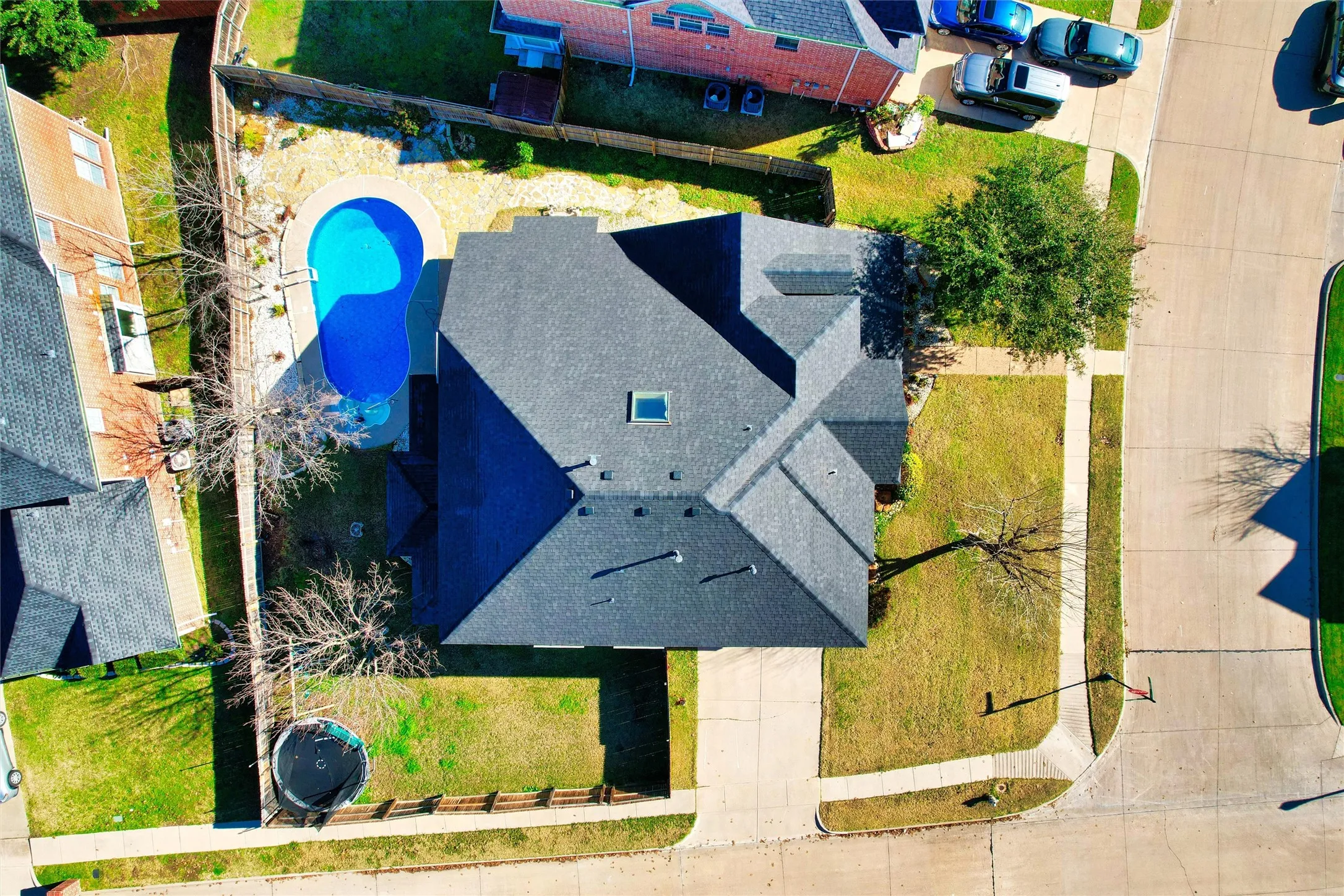 Shingled roof, skylight, concrete driveway, concrete sidewalks, and a fenced backyard with a pool