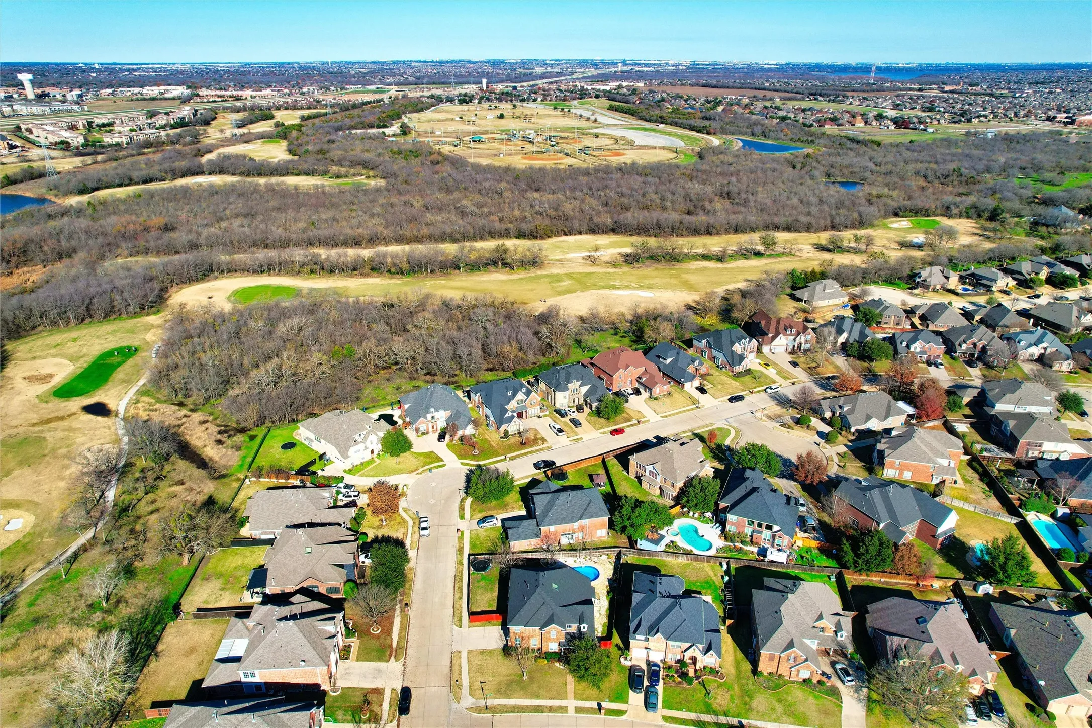 Residential community with a golf course, surrounded by natural land, and featuring multiple homes with swimming pools