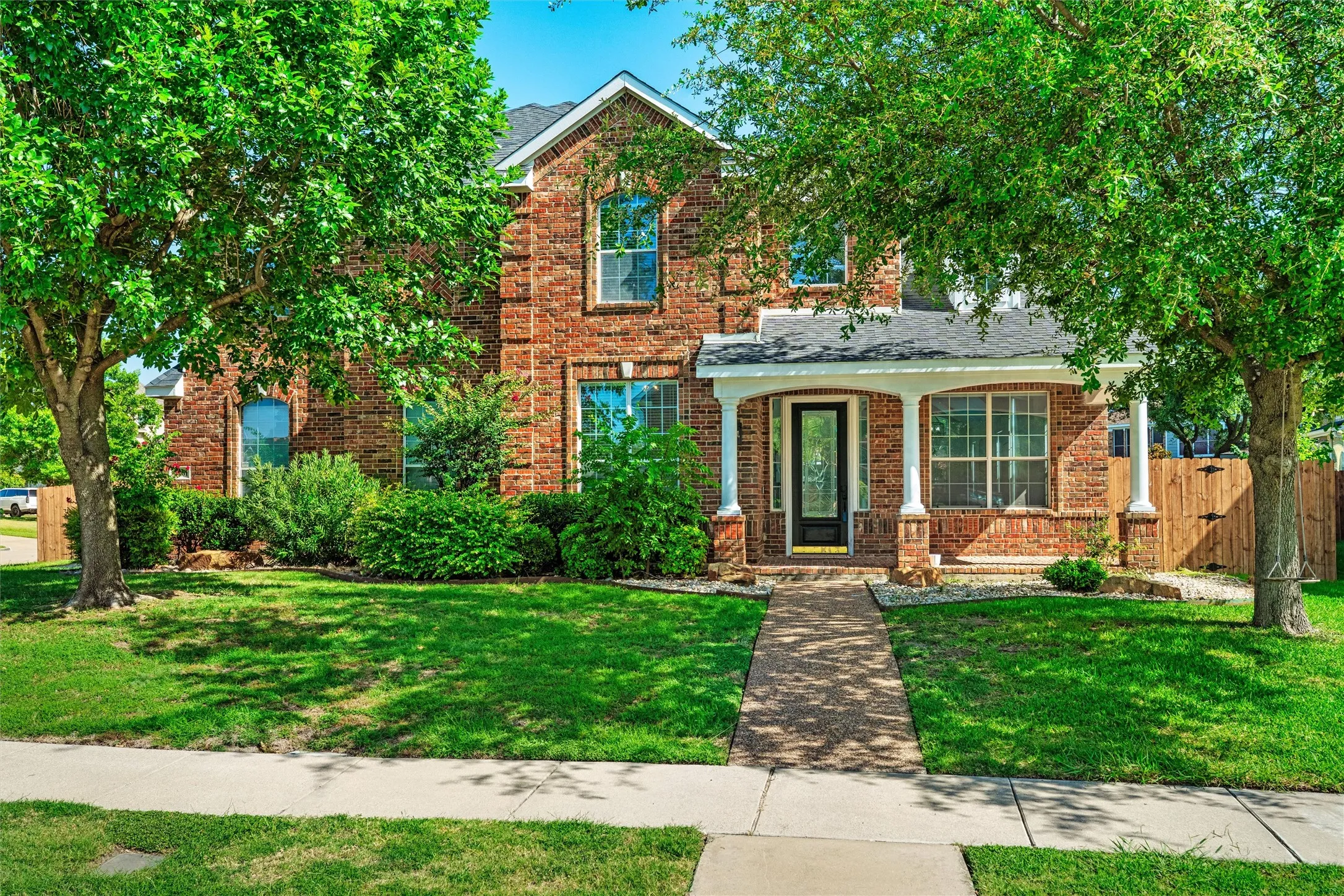 Brick facade with white trim, covered front entry porch, arched window accents, and a paved walkway