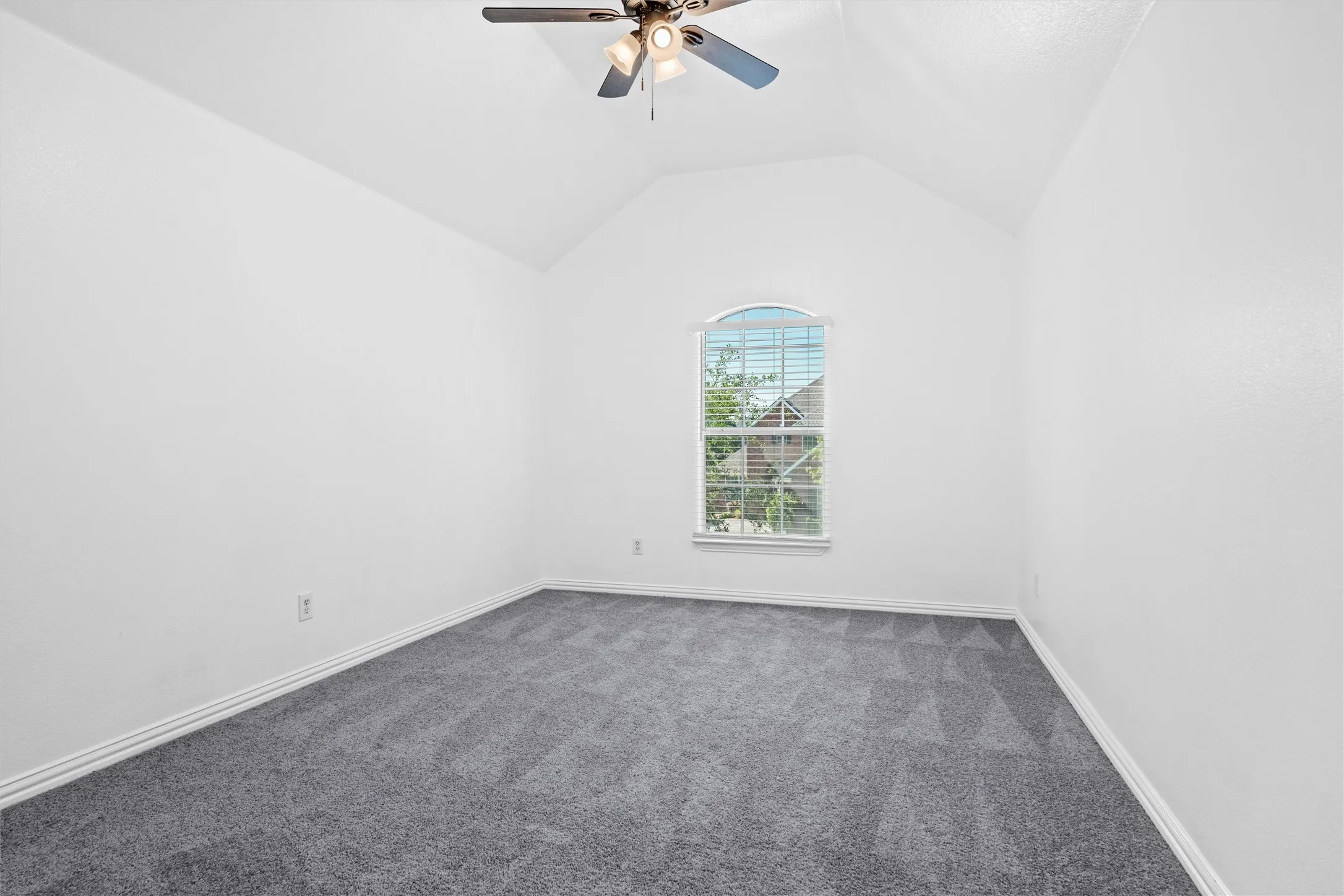 Vaulted ceiling with a ceiling fan, arched window, and patterned carpeting