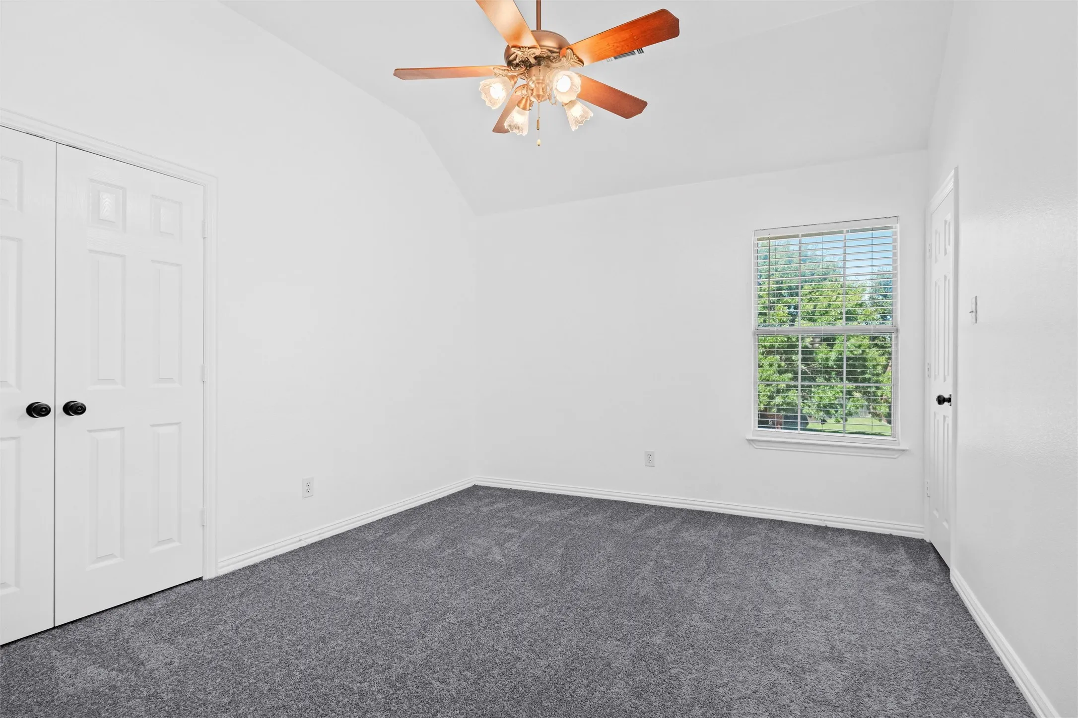 Vaulted ceiling with a ceiling fan light fixture, window with horizontal blinds, and gray carpet flooring