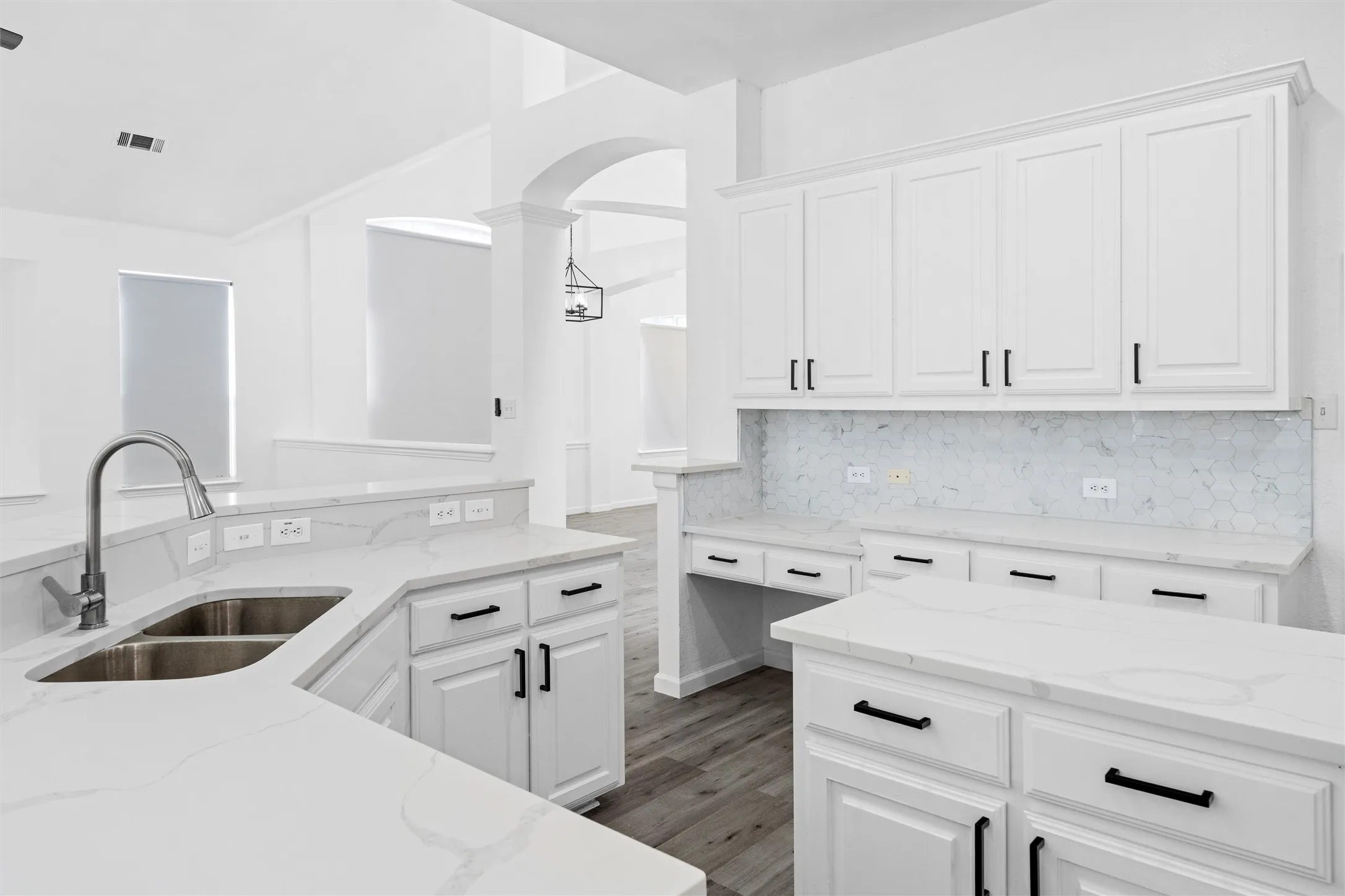 White cabinetry with black hardware, stone countertops, a tile backsplash, a double basin stainless steel sink, and wood-finish flooring