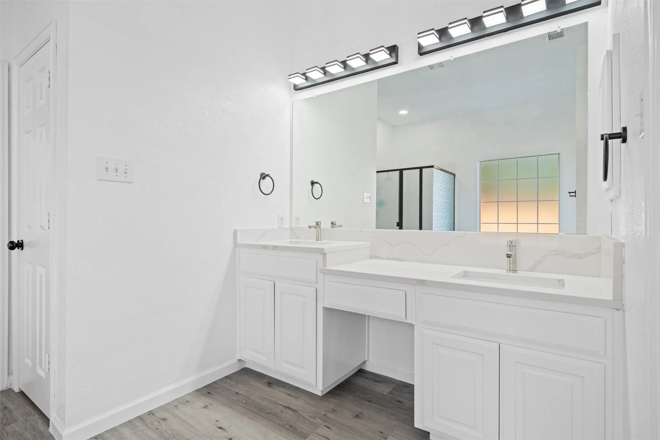 Dual vanity with white cabinetry and integrated sinks, complemented by light-toned wood-finish flooring