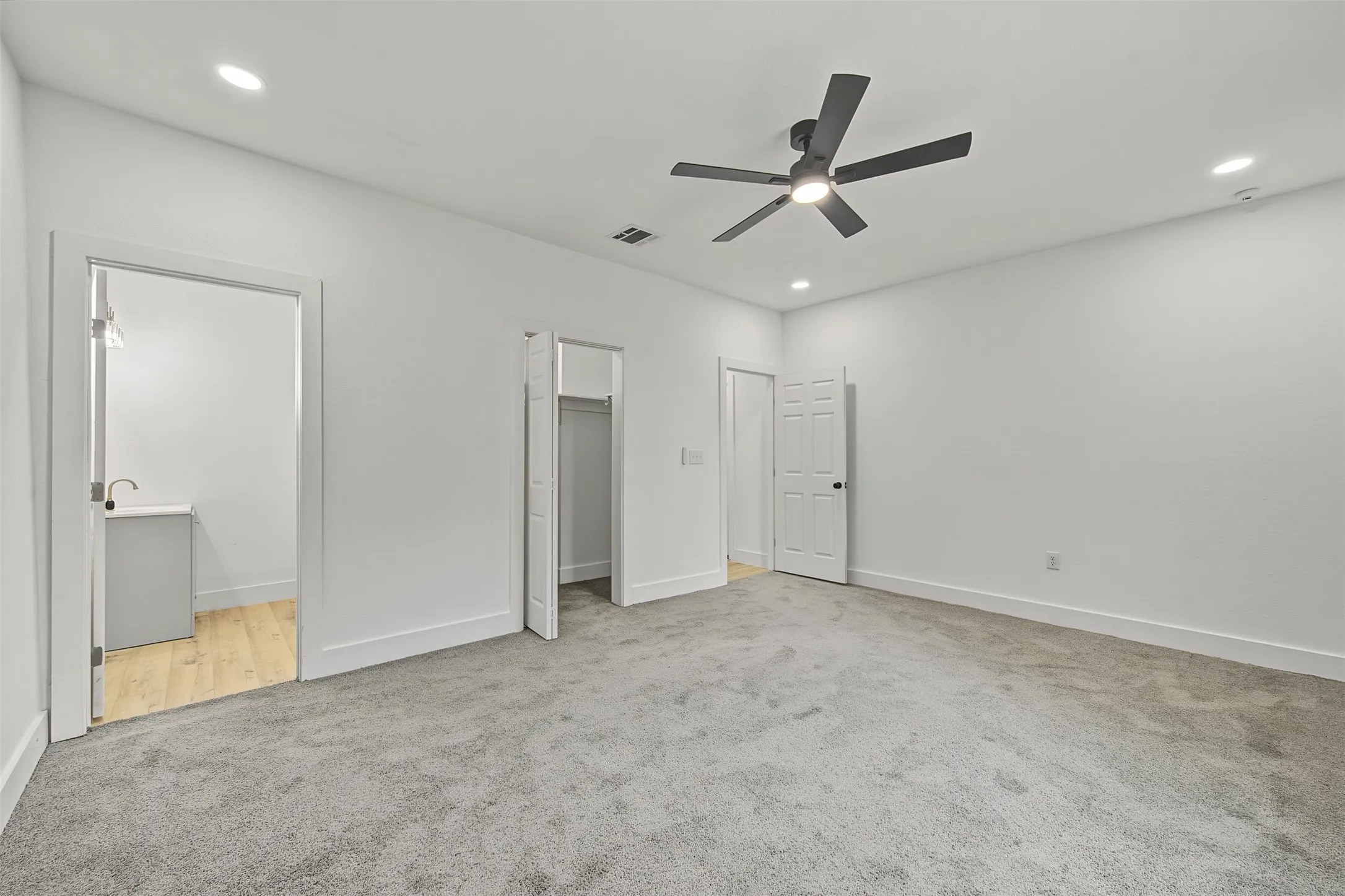 Recessed lighting, ceiling fan with integrated light, light gray carpeting, crisp white walls, and a white panel door