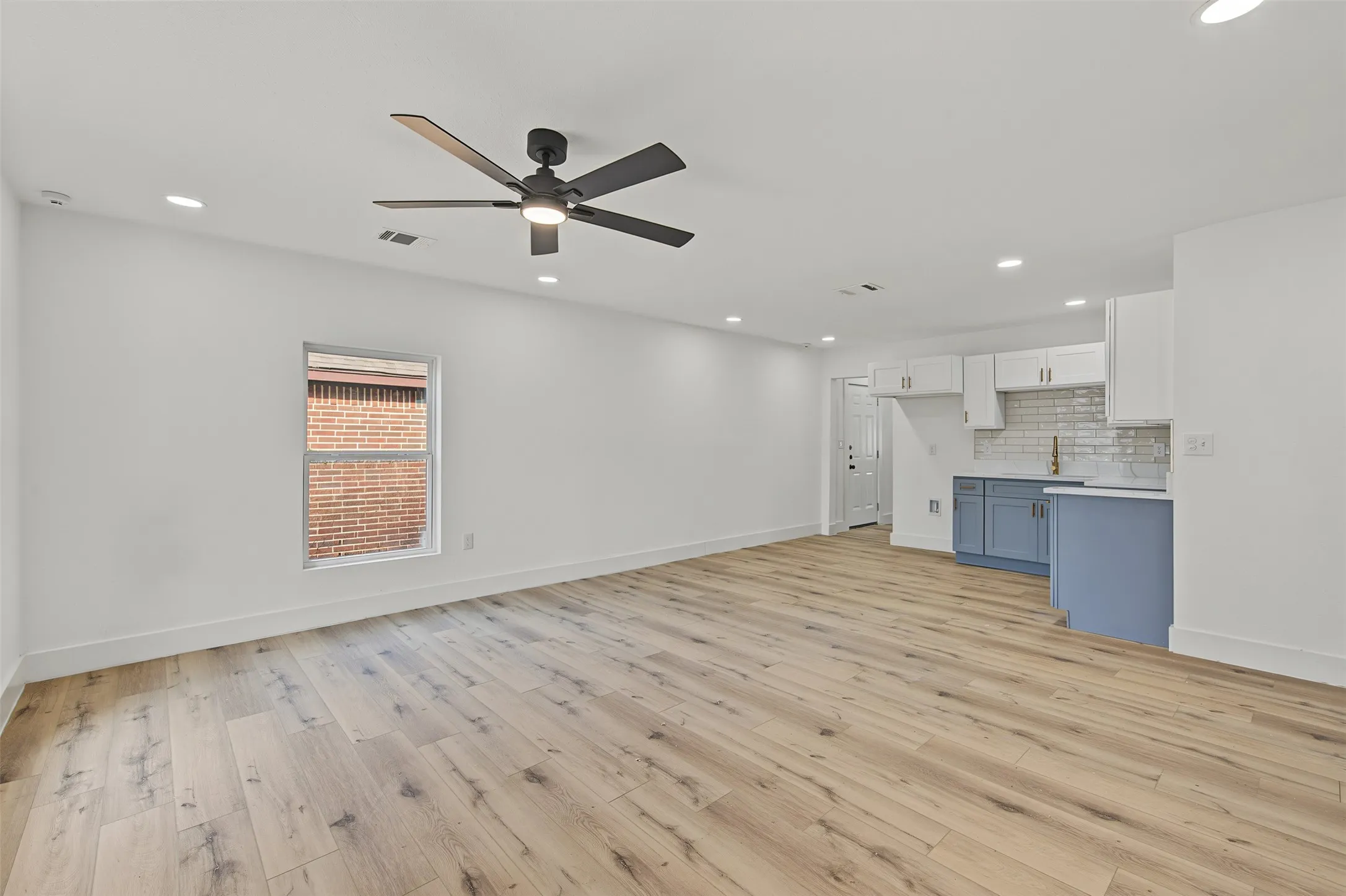 Open-concept living space with wood-finish flooring, recessed lighting, a ceiling fan, and a kitchen featuring white upper cabinetry, blue lower cabinetry, and a subway tile backsplash