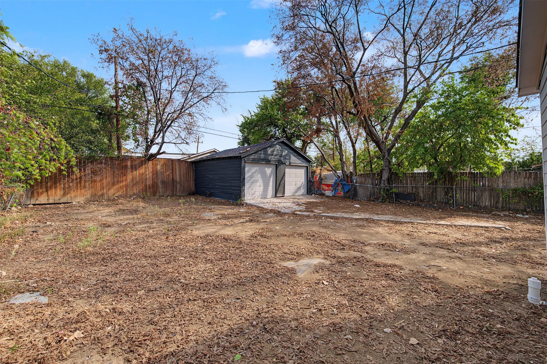 Expansive backyard area featuring a detached two-car garage with overhead doors, a wood privacy fence, and mature trees