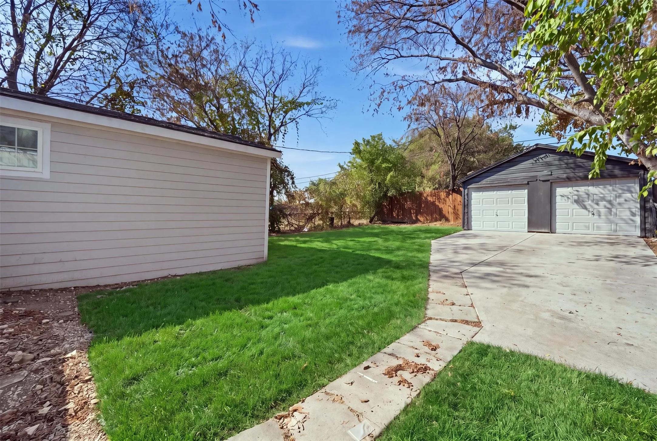 Expansive yard featuring a detached two-car garage, concrete driveway, and mature trees