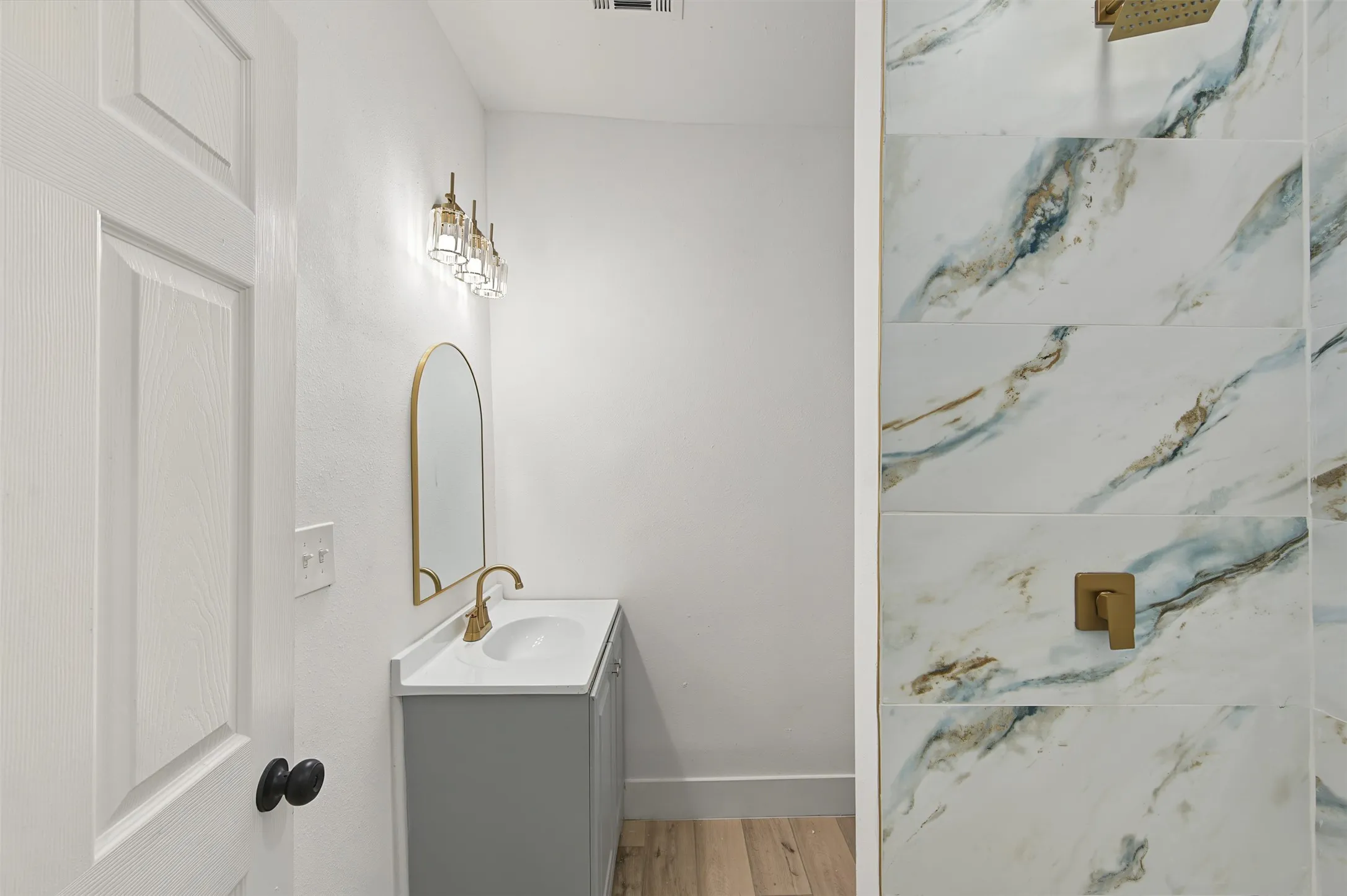 Vanity with a white countertop and gold-finish faucet, arched gold-finish mirror, and a three-bulb wall sconce