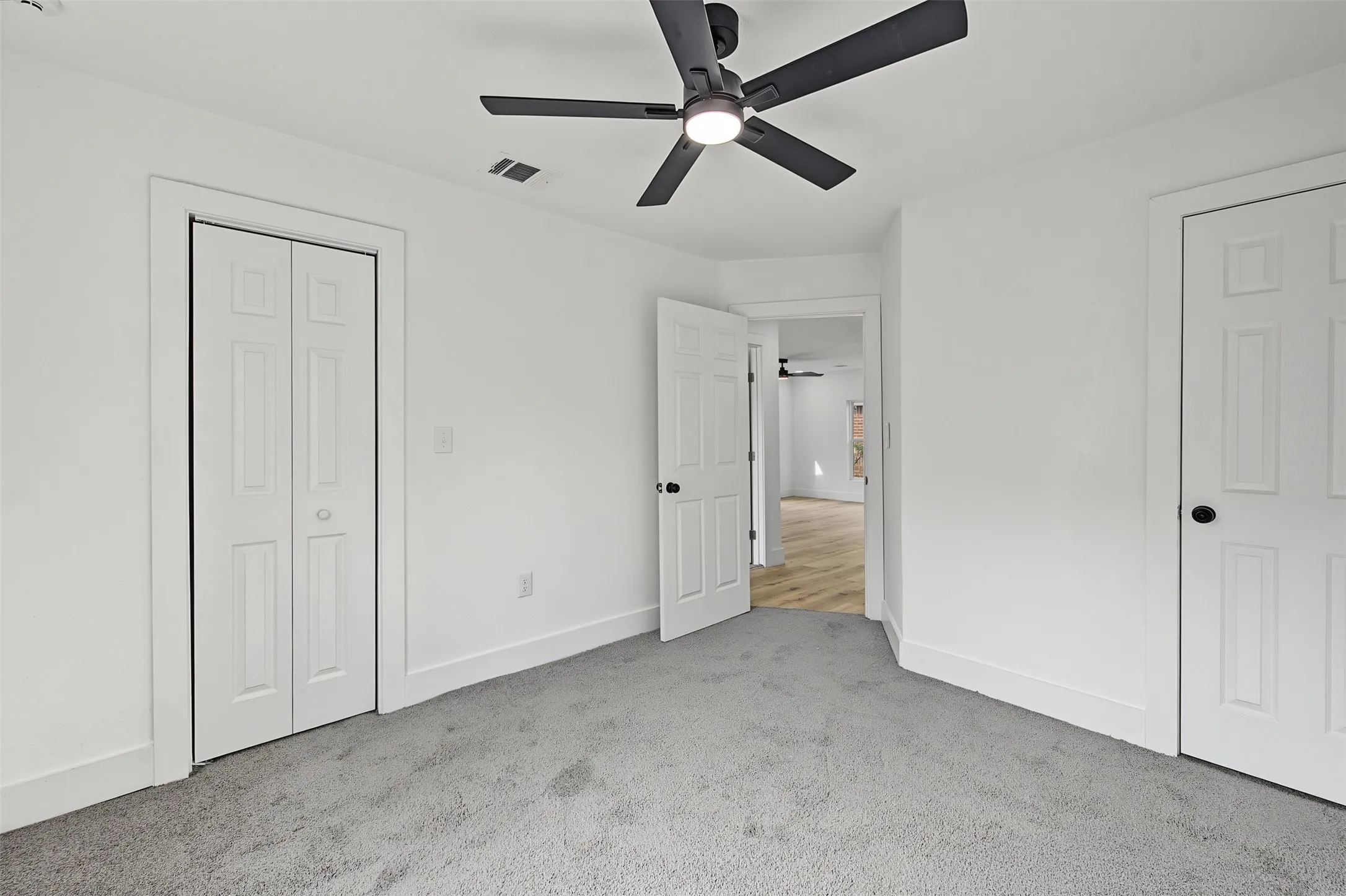 Gray carpet flooring, white painted walls, white trim, white paneled doors, and a ceiling fan with integrated lighting