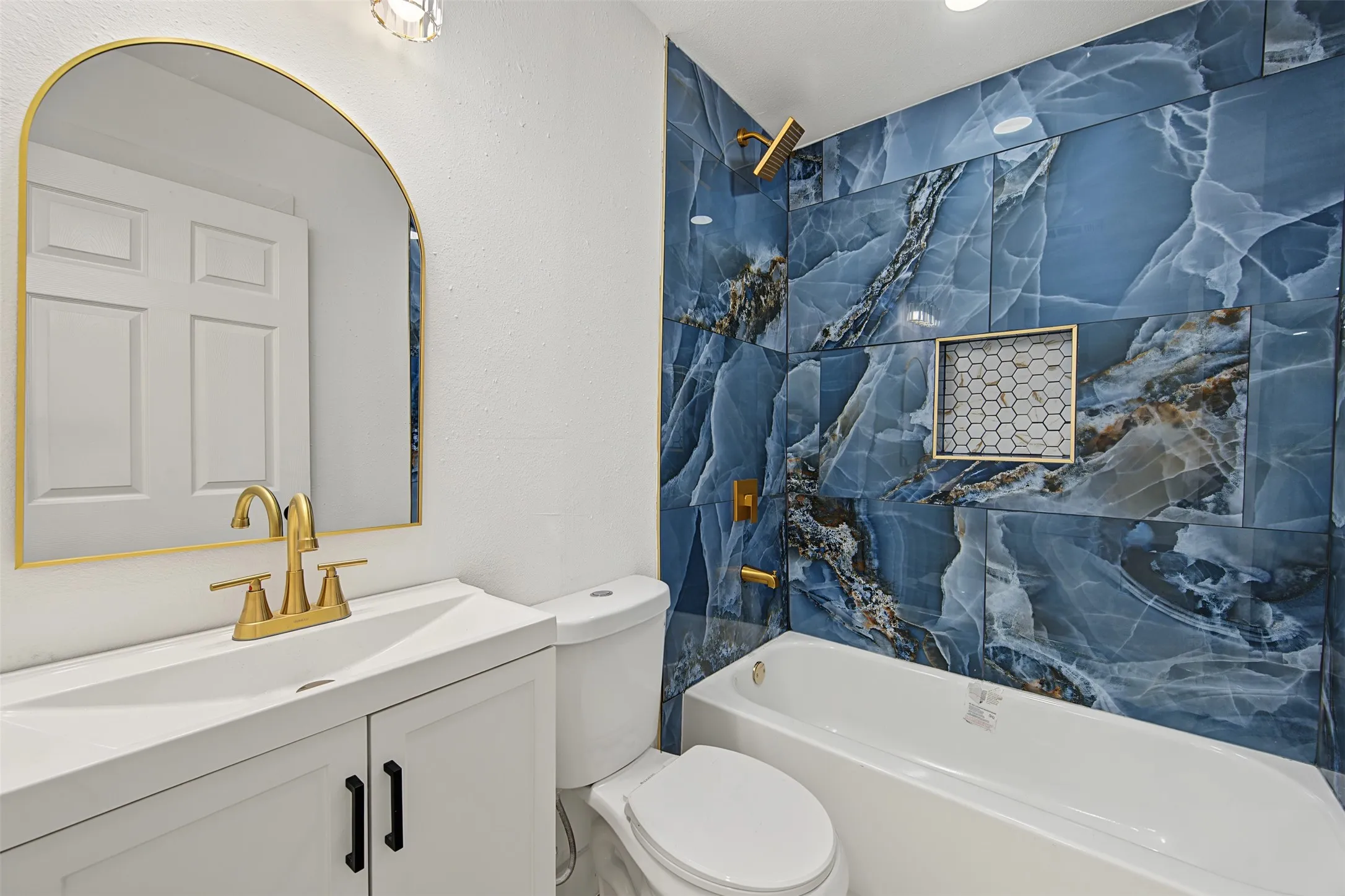 White vanity with a single basin, gold-finish faucet, and black pulls
