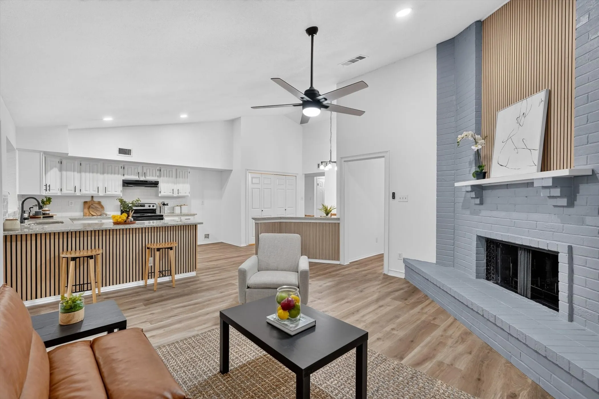 Vaulted ceiling living area featuring a brick fireplace with a mantel, wood-finish flooring, and a ceiling fan