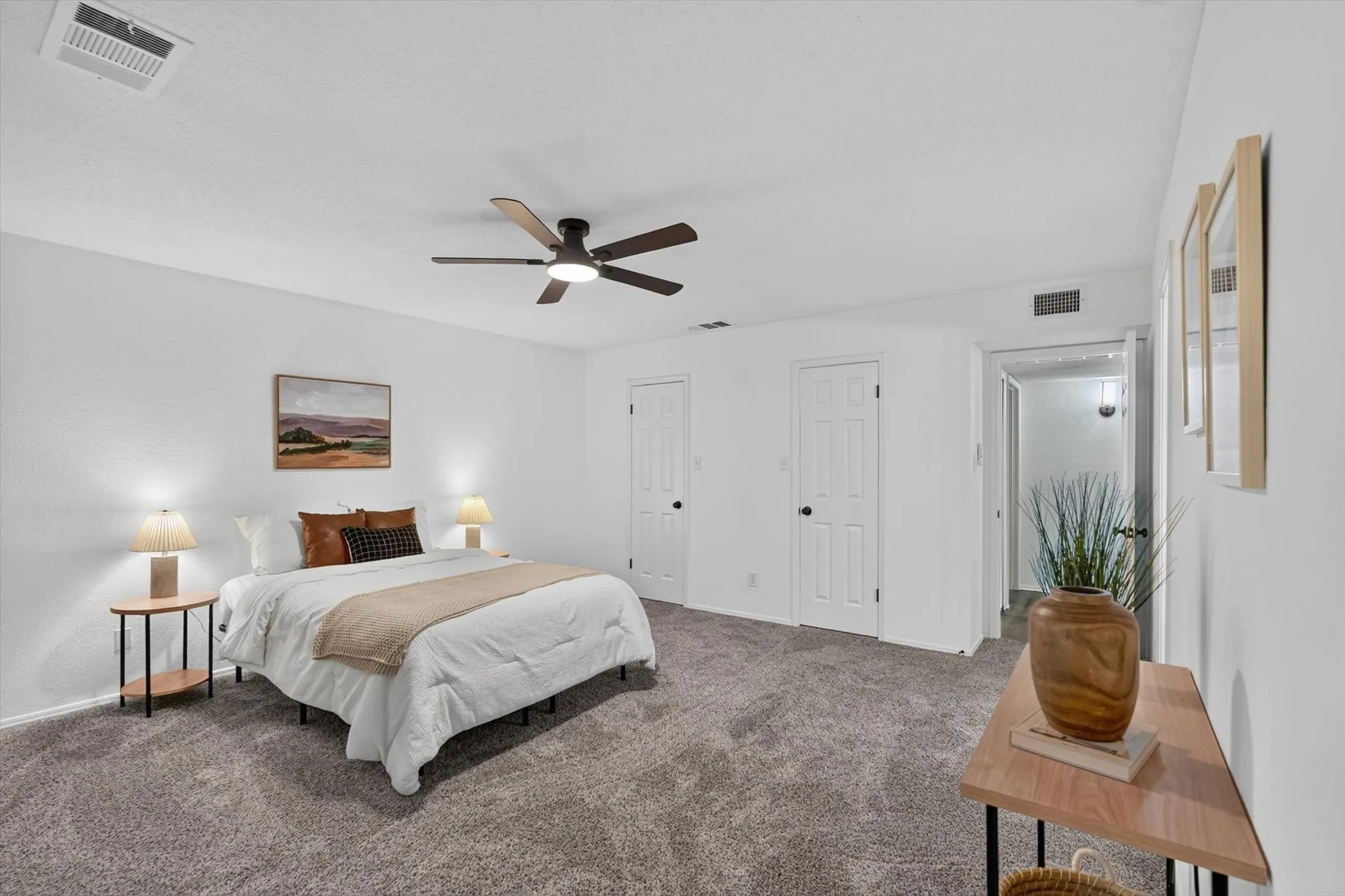 Spacious bedroom with grey textured carpeting, white walls, and a contemporary ceiling fan