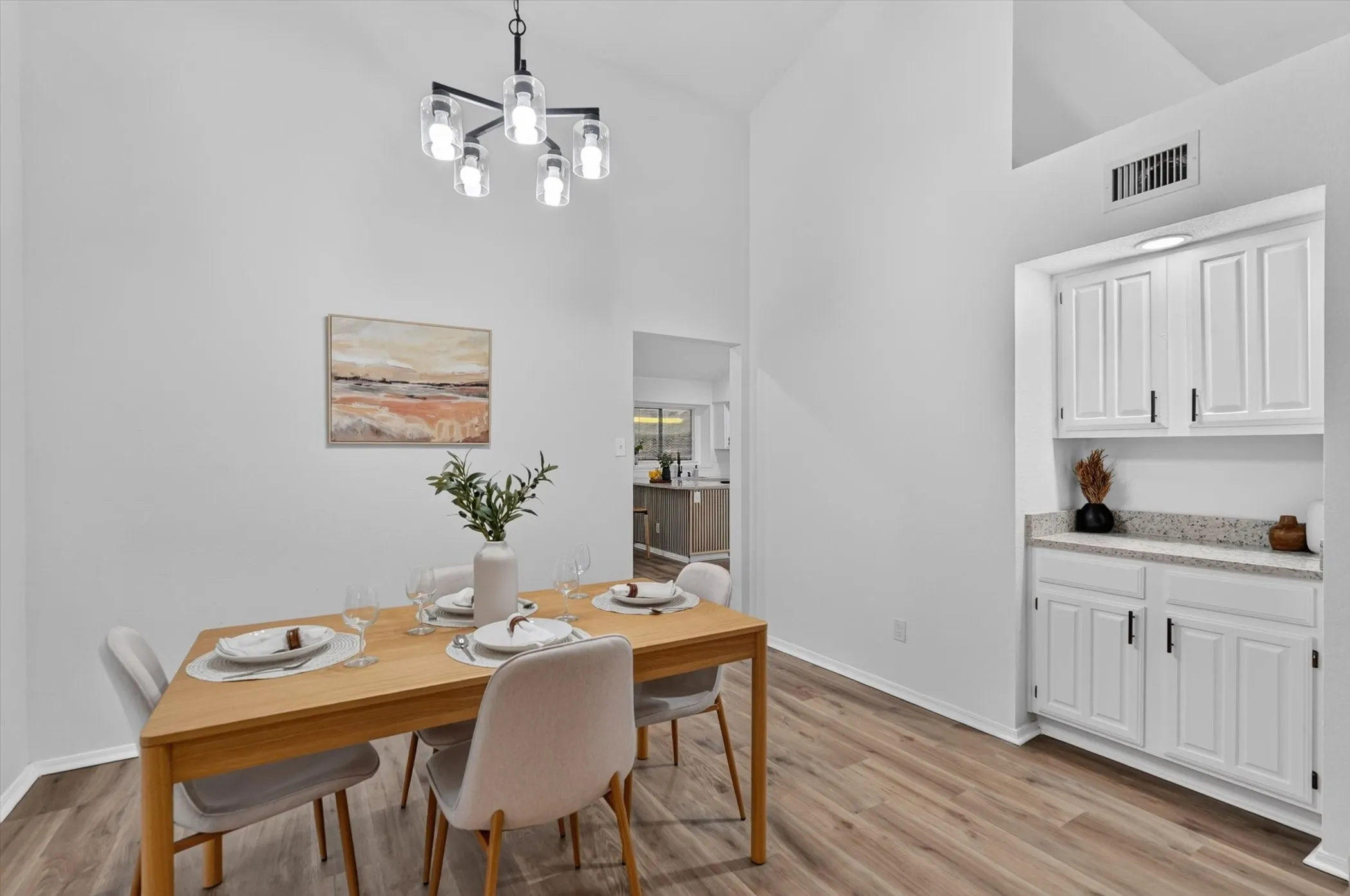 Vaulted ceilings, wood-finish flooring, built-in cabinetry with granite-look countertop, and a contemporary chandelier