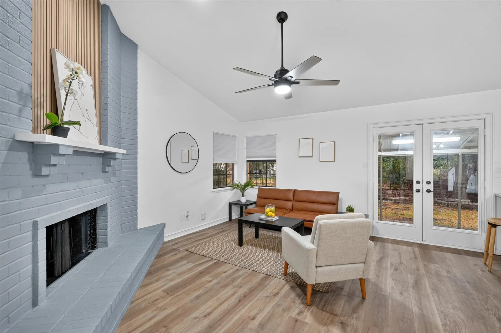 Vaulted ceiling with a ceiling fan, brick fireplace with a wood mantel, wood-finish flooring, and French doors