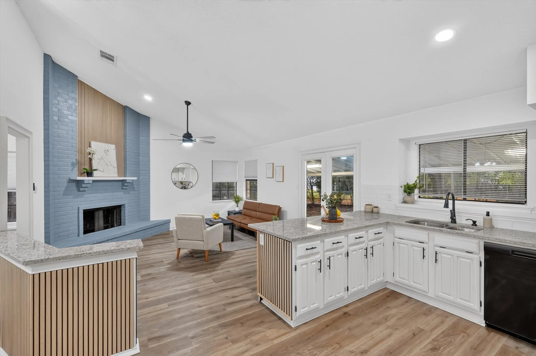 Vaulted ceiling, wood-finish flooring, fireplace with mantle, white cabinetry, and light-toned countertops