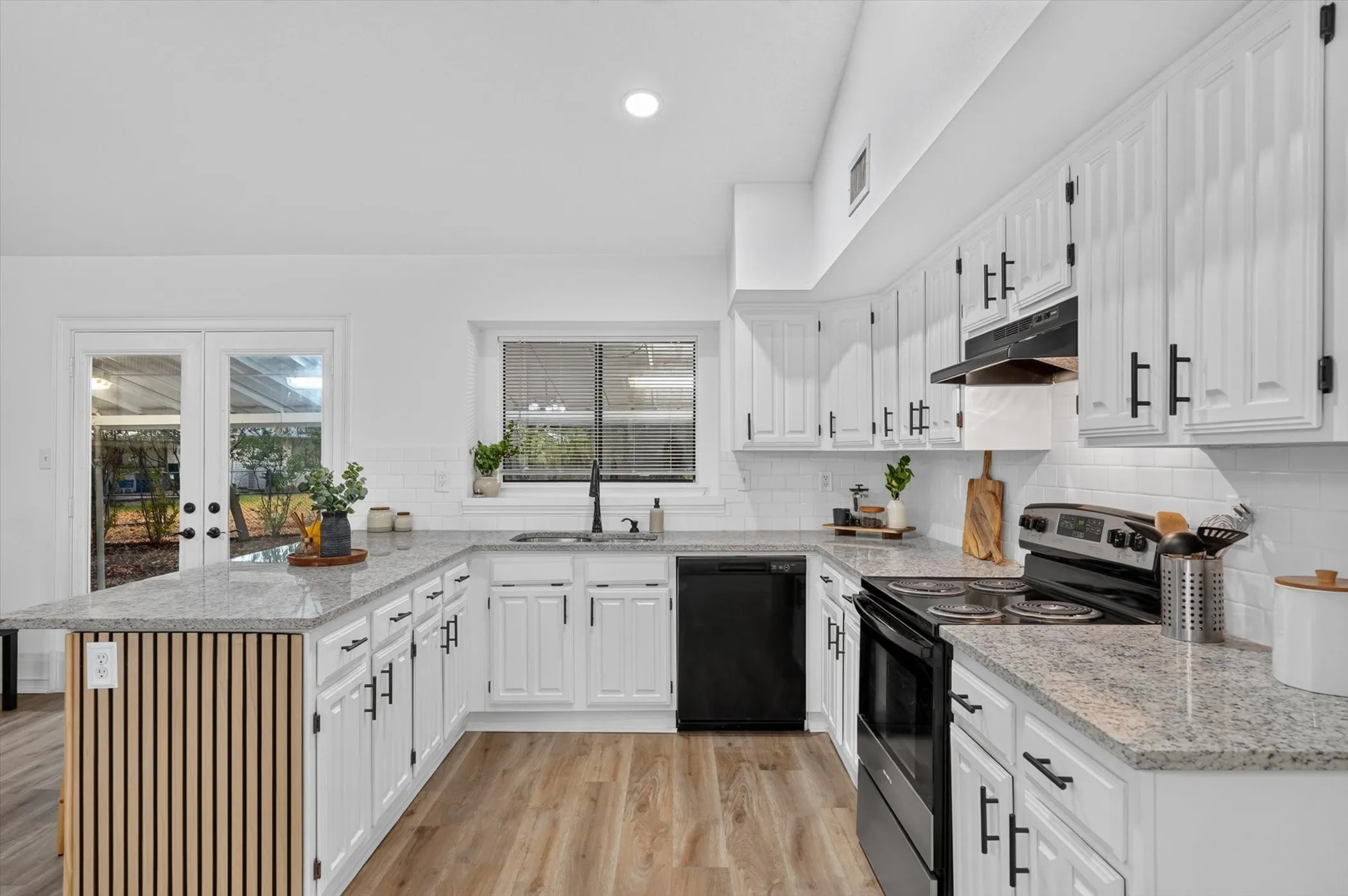 White cabinetry with black hardware, stone countertops, wood-finish flooring, and subway tile backsplash