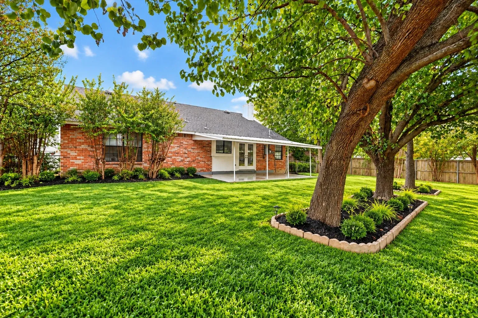 Brick ranch home with a sprawling manicured lawn and mature shade trees featuring natural canopy coverage