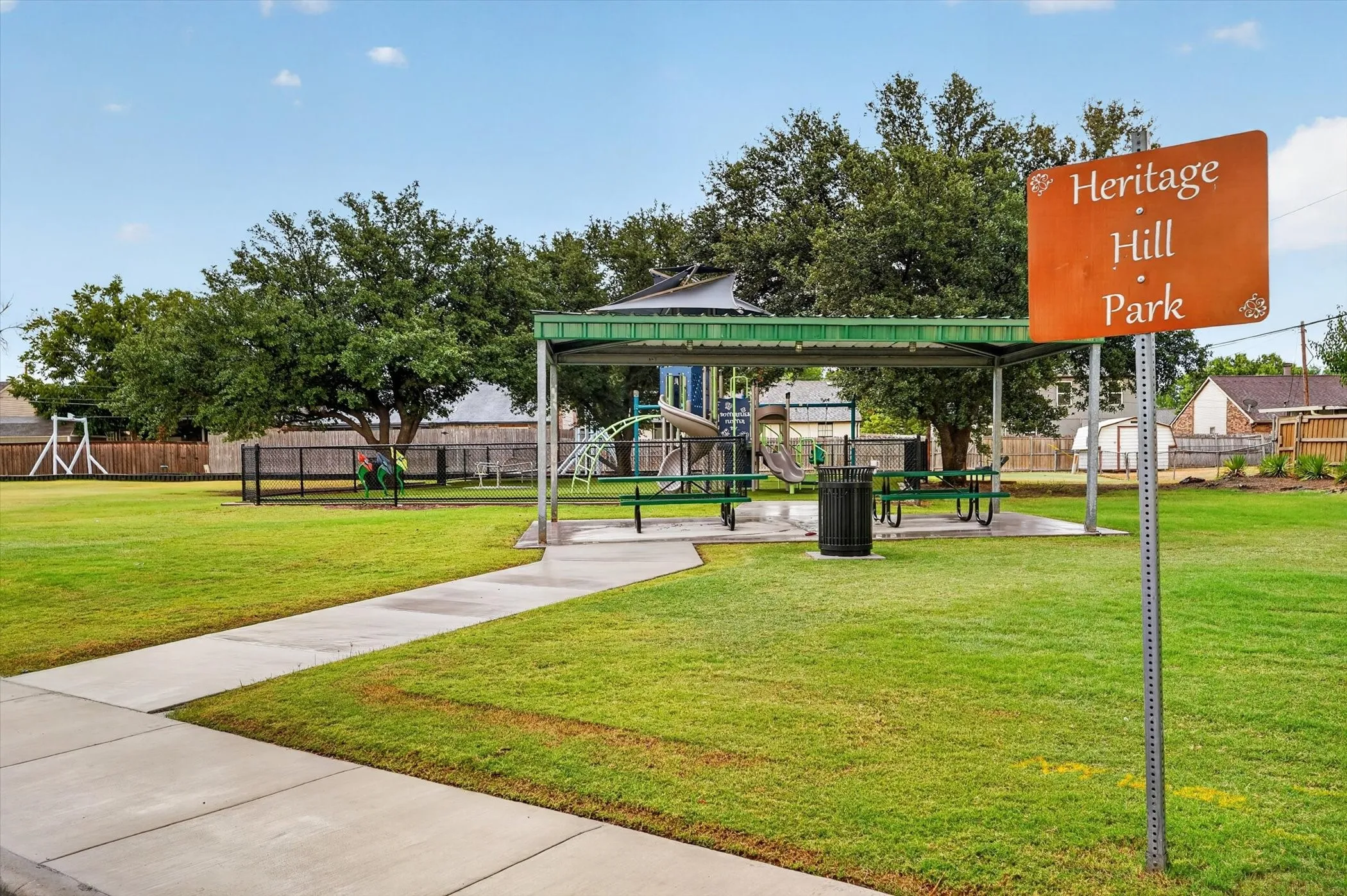 Heritage Hill Park featuring a shaded playground structure, picnic tables, and a paved pathway