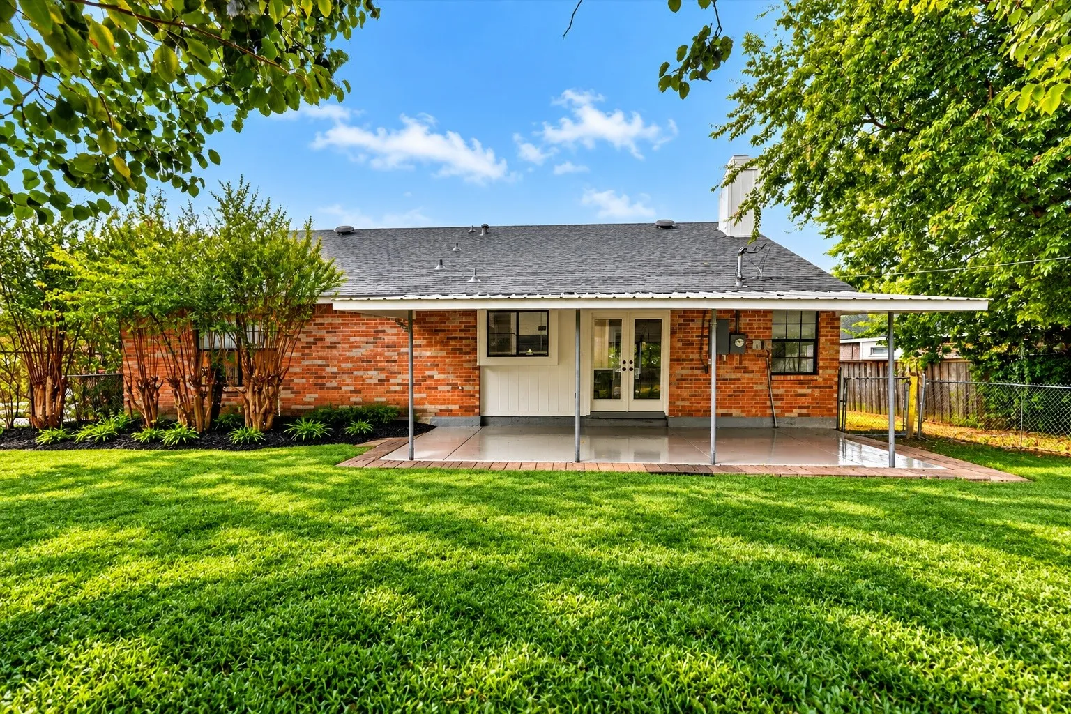 Expansive green lawn, brick exterior, covered patio, white double doors, and mature landscaping