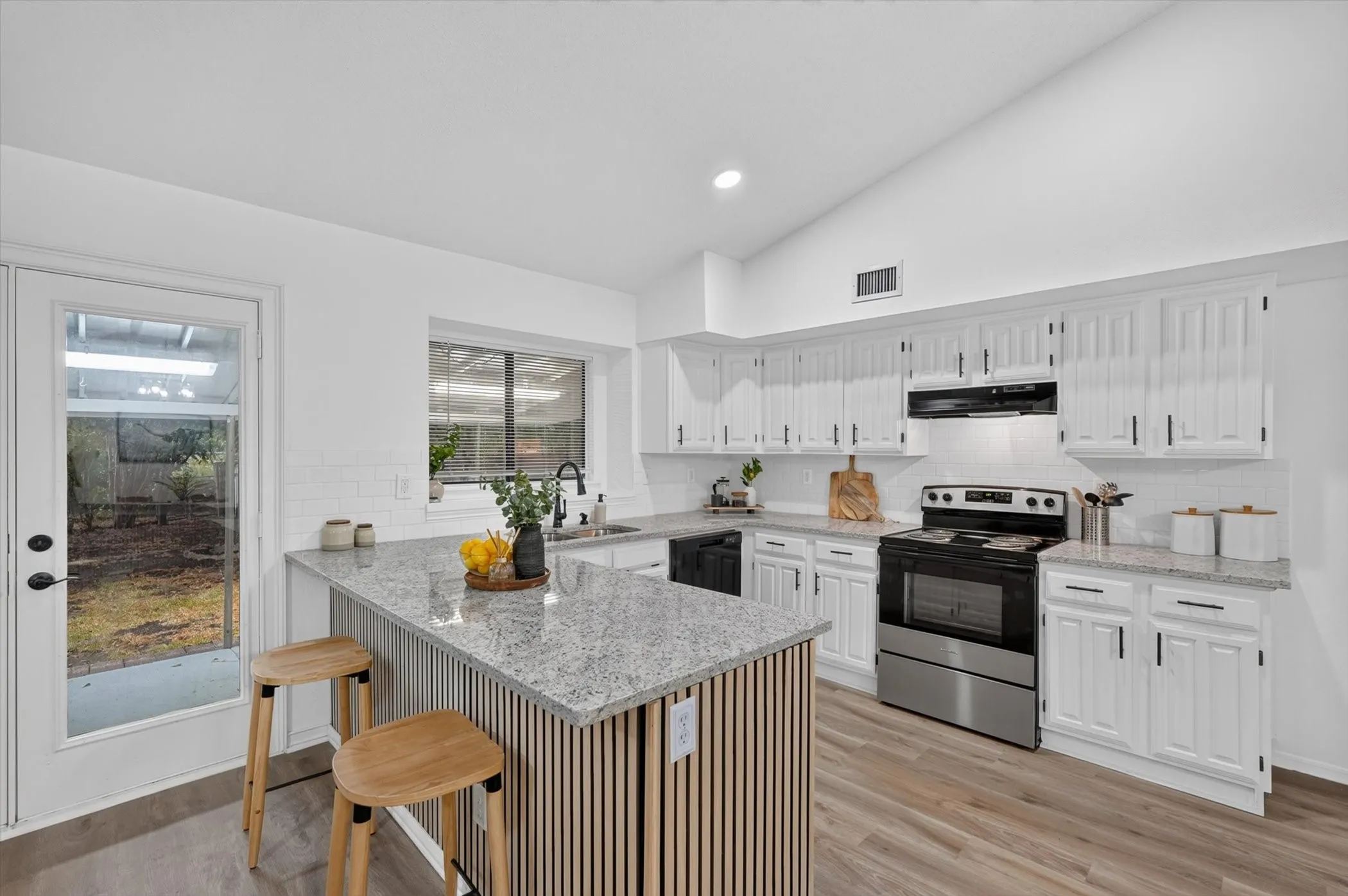 Kitchen featuring vaulted ceilings, white cabinetry, a center island with a wood-slat base, stainless steel appliances, and a glass-paneled exterior door