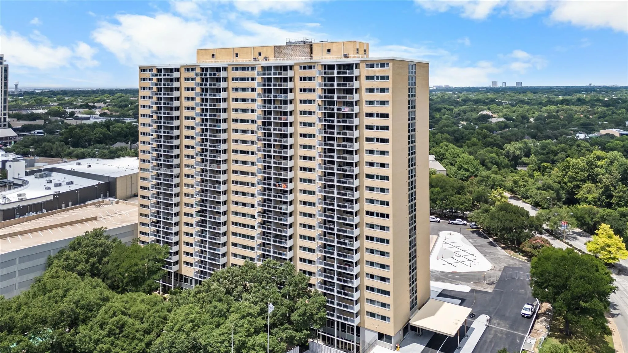 High-rise building with multiple private balconies, a covered entrance, and extensive surrounding tree canopy