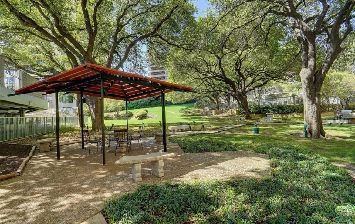 Expansive outdoor area featuring a red metal gazebo, gravel patio, stone benches, and mature trees