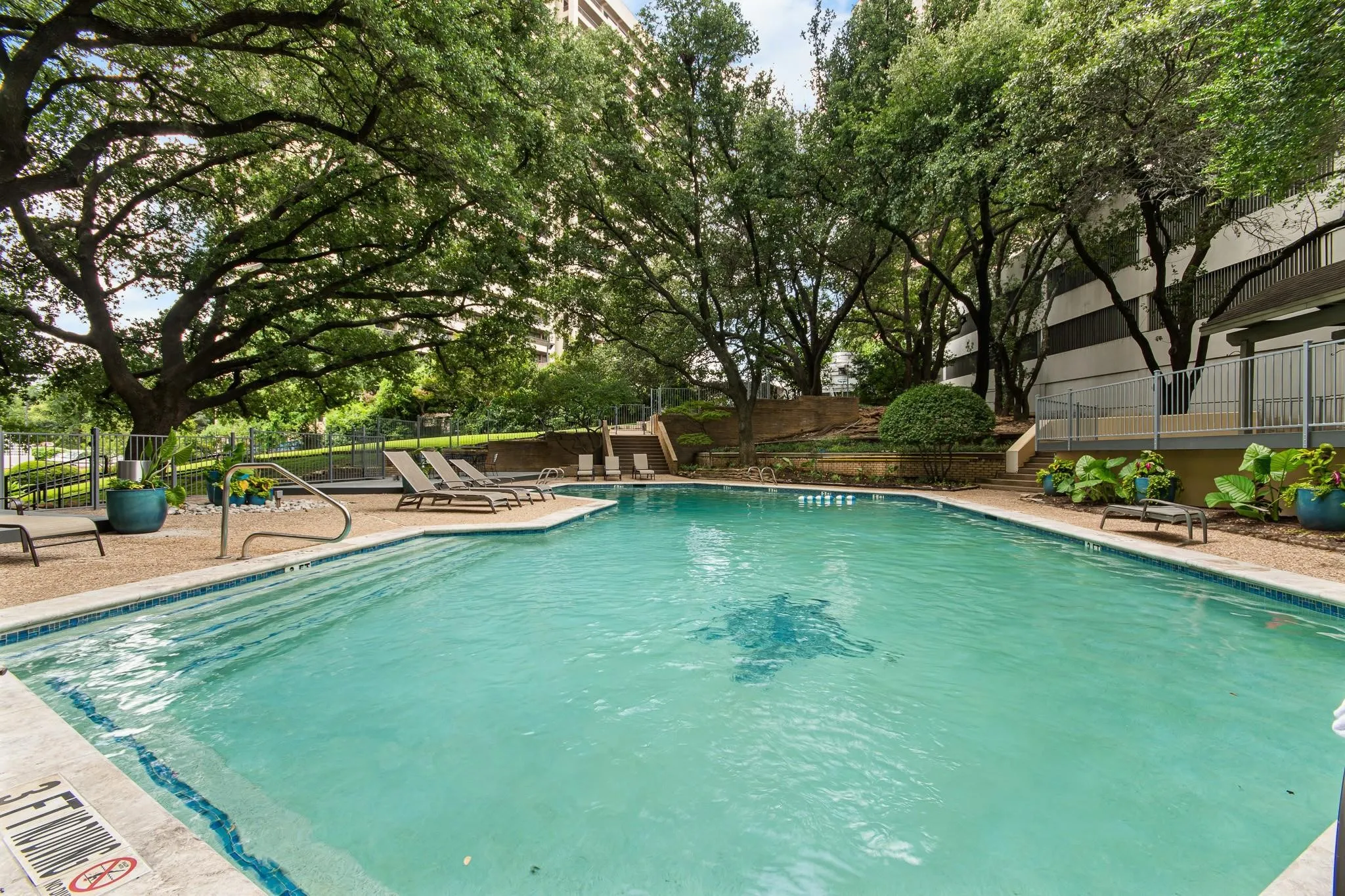 Outdoor swimming pool with integrated steps, surrounded by a pebble-finish deck and mature trees