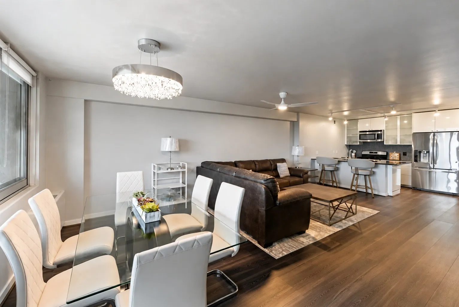 Open-concept living space featuring wood-finish flooring, a modern kitchen with stainless steel appliances, a kitchen island with seating, and track lighting