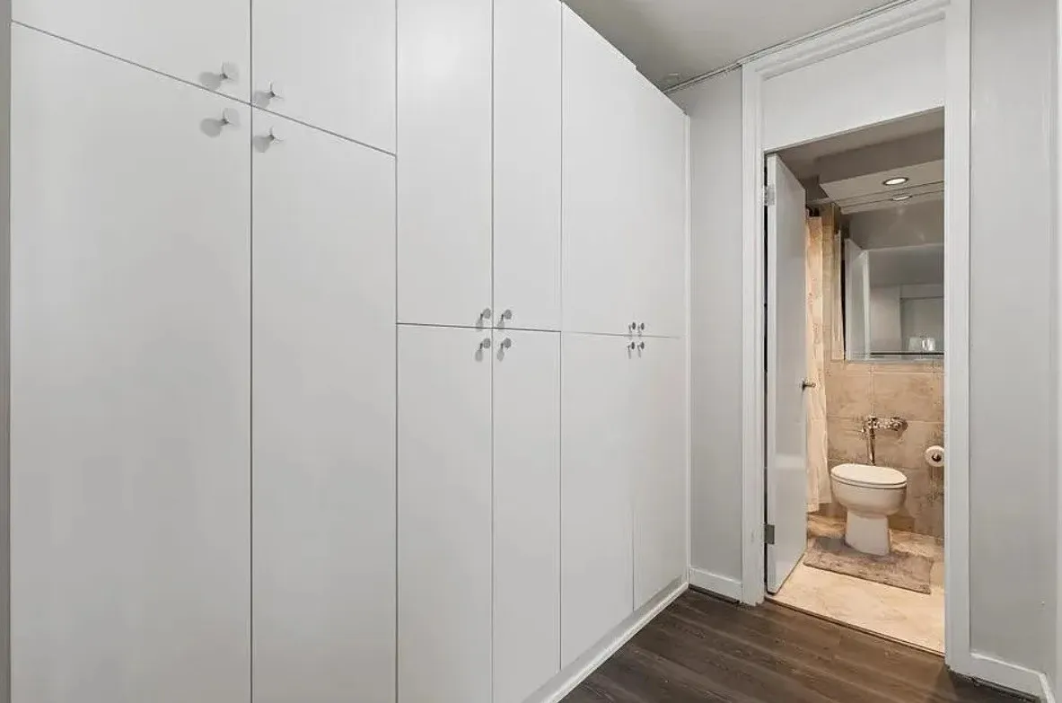 Extensive built-in white cabinetry with polished chrome hardware, wood-finish flooring, and a powder room featuring a toilet and natural stone tile
