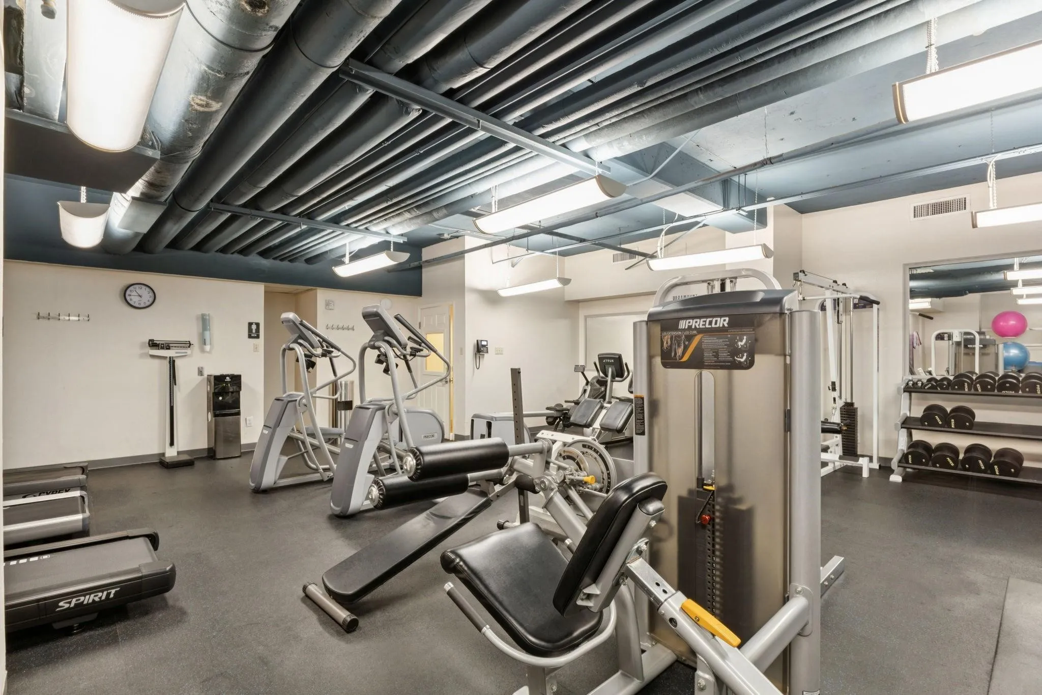Fitness center featuring exposed industrial-style ceiling, track lighting, rubber flooring, and a variety of exercise equipment