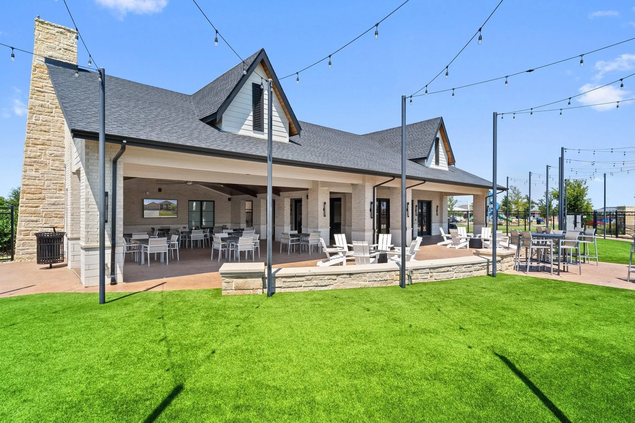 Expansive outdoor entertainment community area featuring a covered patio, multiple seating arrangements, string lighting, and a stone-clad exterior with a prominent chimney