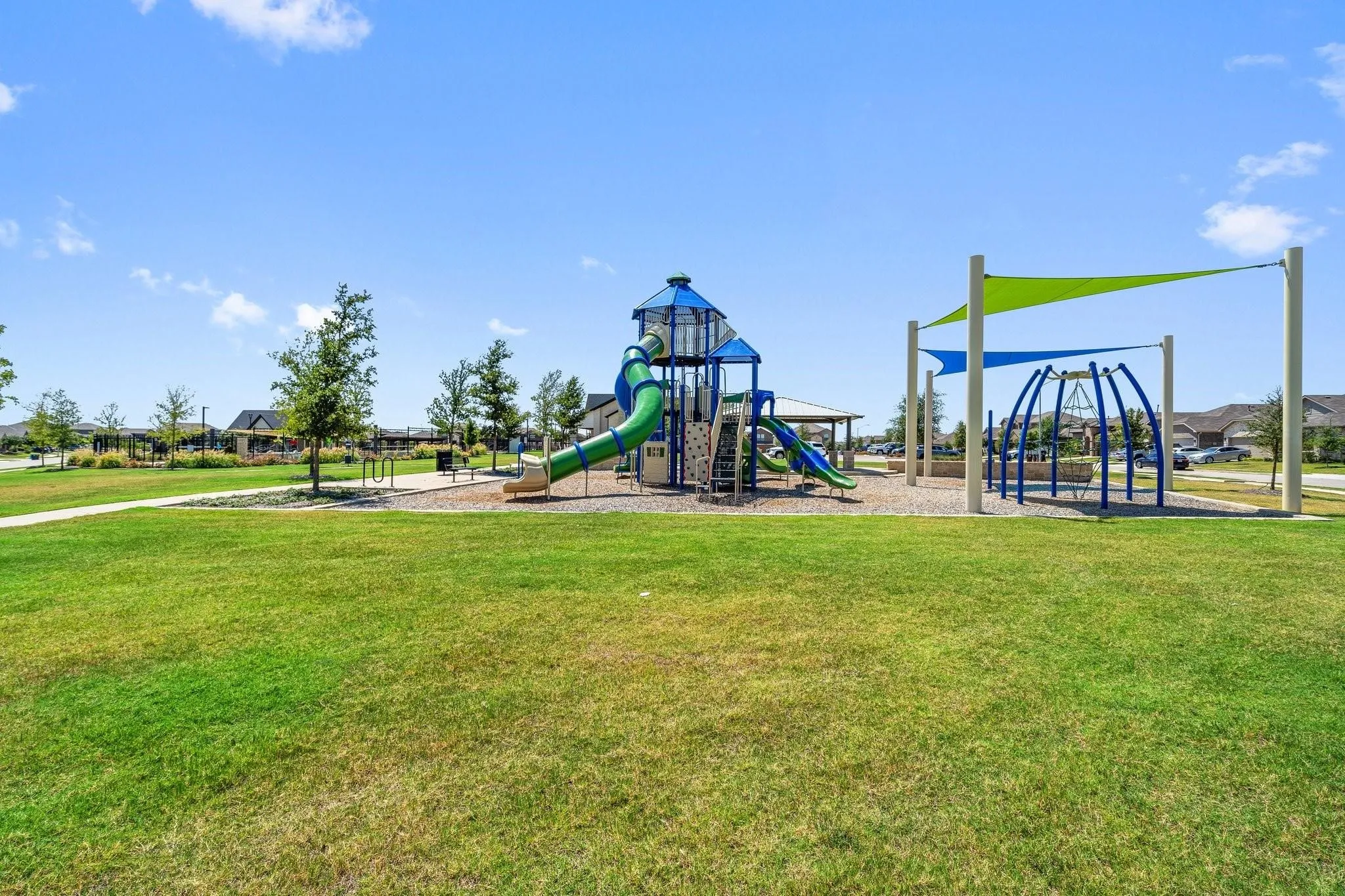 Expansive green space featuring a playground with a slide, climbing structures, and shade canopies