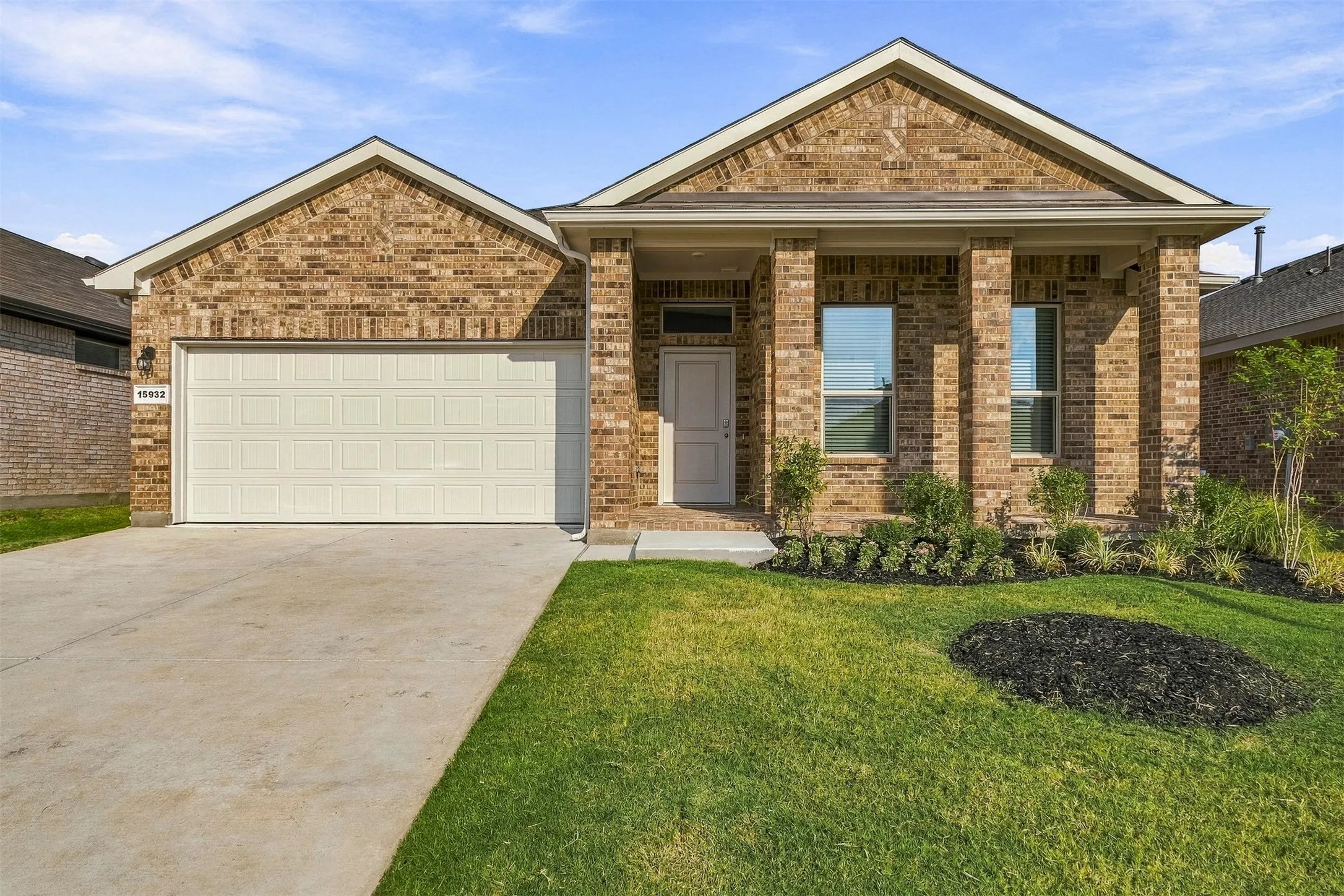 Brick exterior with a gabled roofline, covered entry, attached garage, concrete driveway, and landscaped front yard