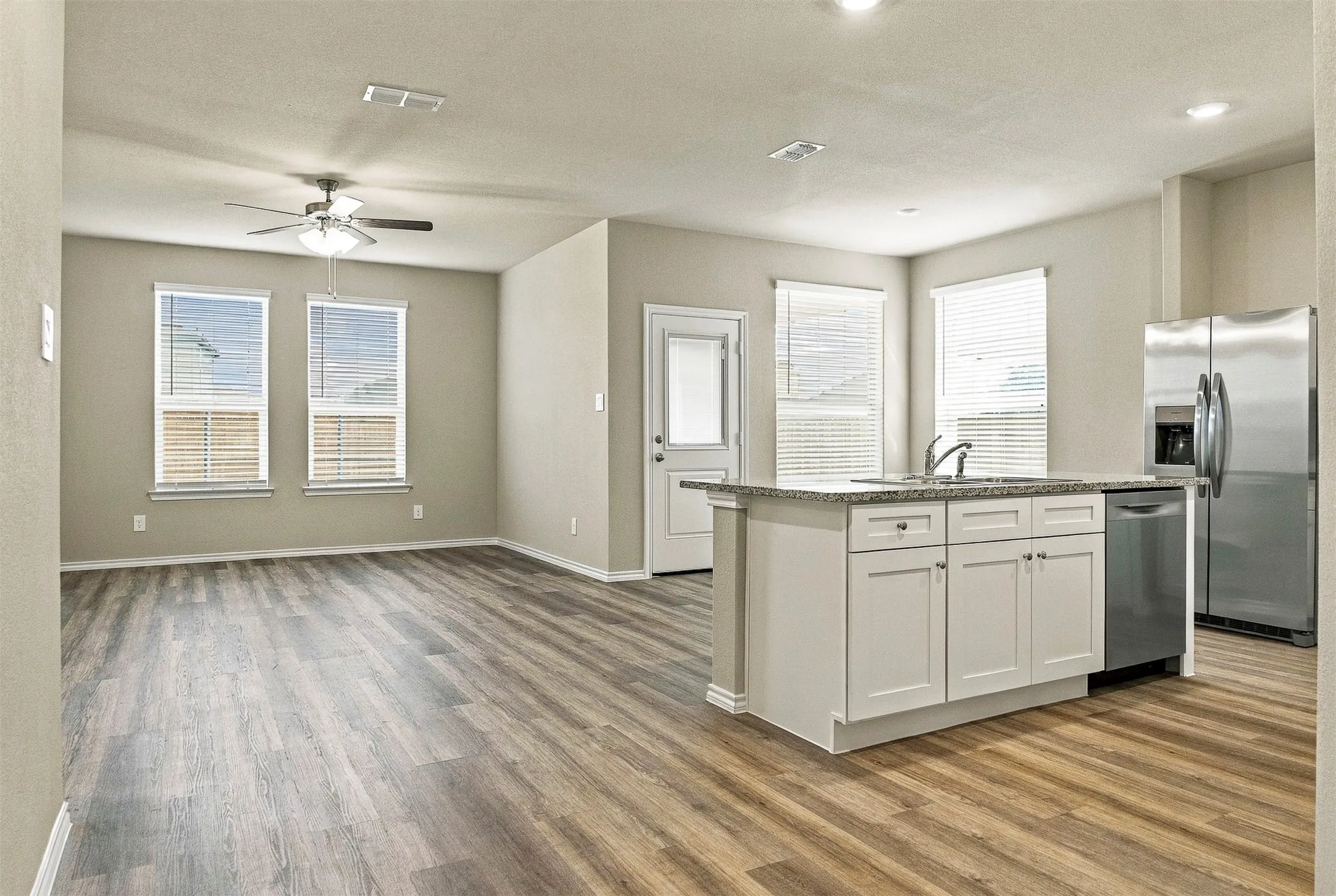 Open-concept living area featuring wood-finish flooring, a ceiling fan, and multiple windows