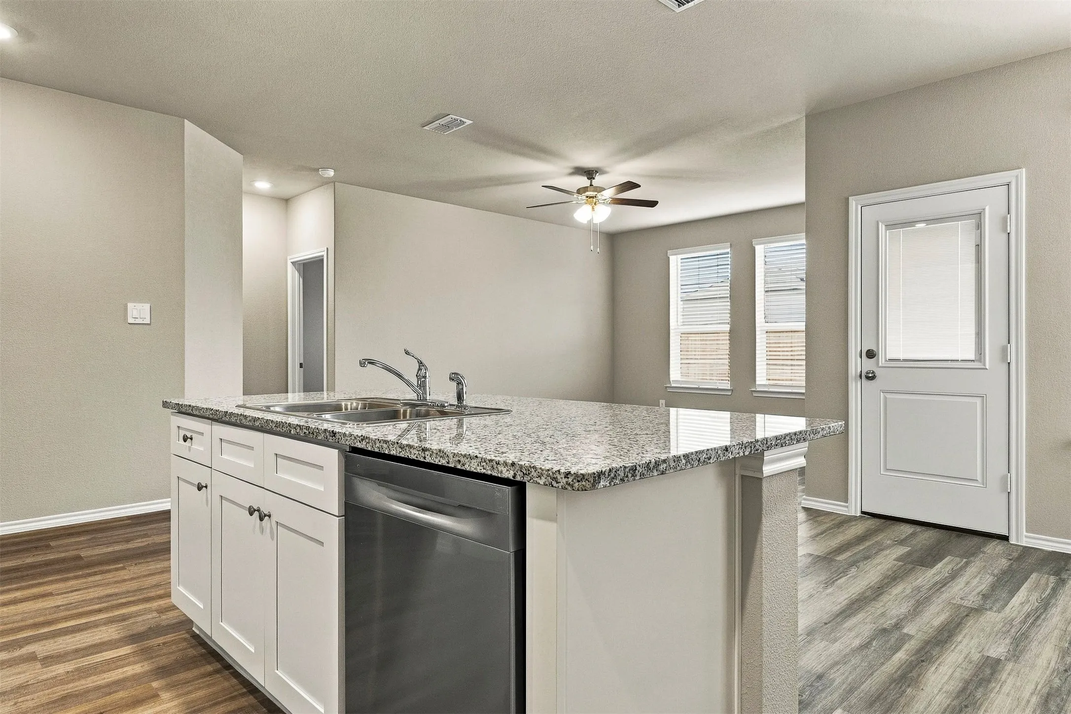 Kitchen island with a double basin stainless steel sink, stainless steel dishwasher, and a light-toned countertop