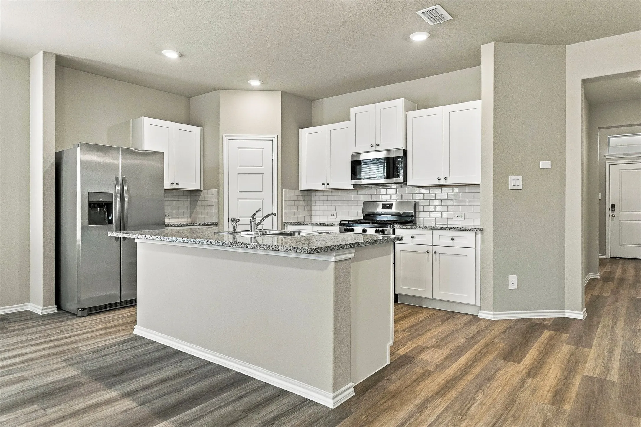 Kitchen featuring an island with a light-toned countertop, stainless steel appliances, white cabinetry, subway tile backsplash, and recessed lighting