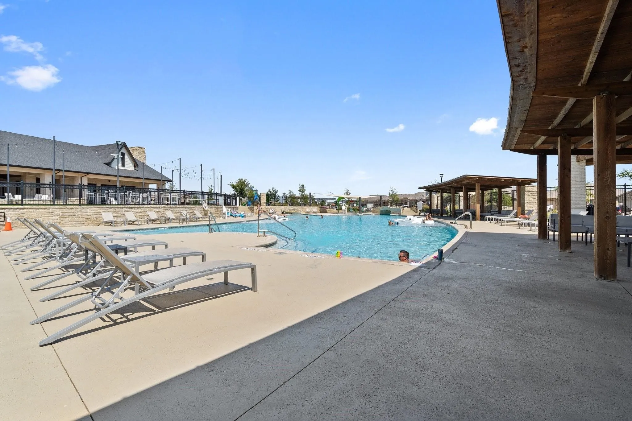 Community swimming pool with a large paved surround and multiple shaded lounge areas