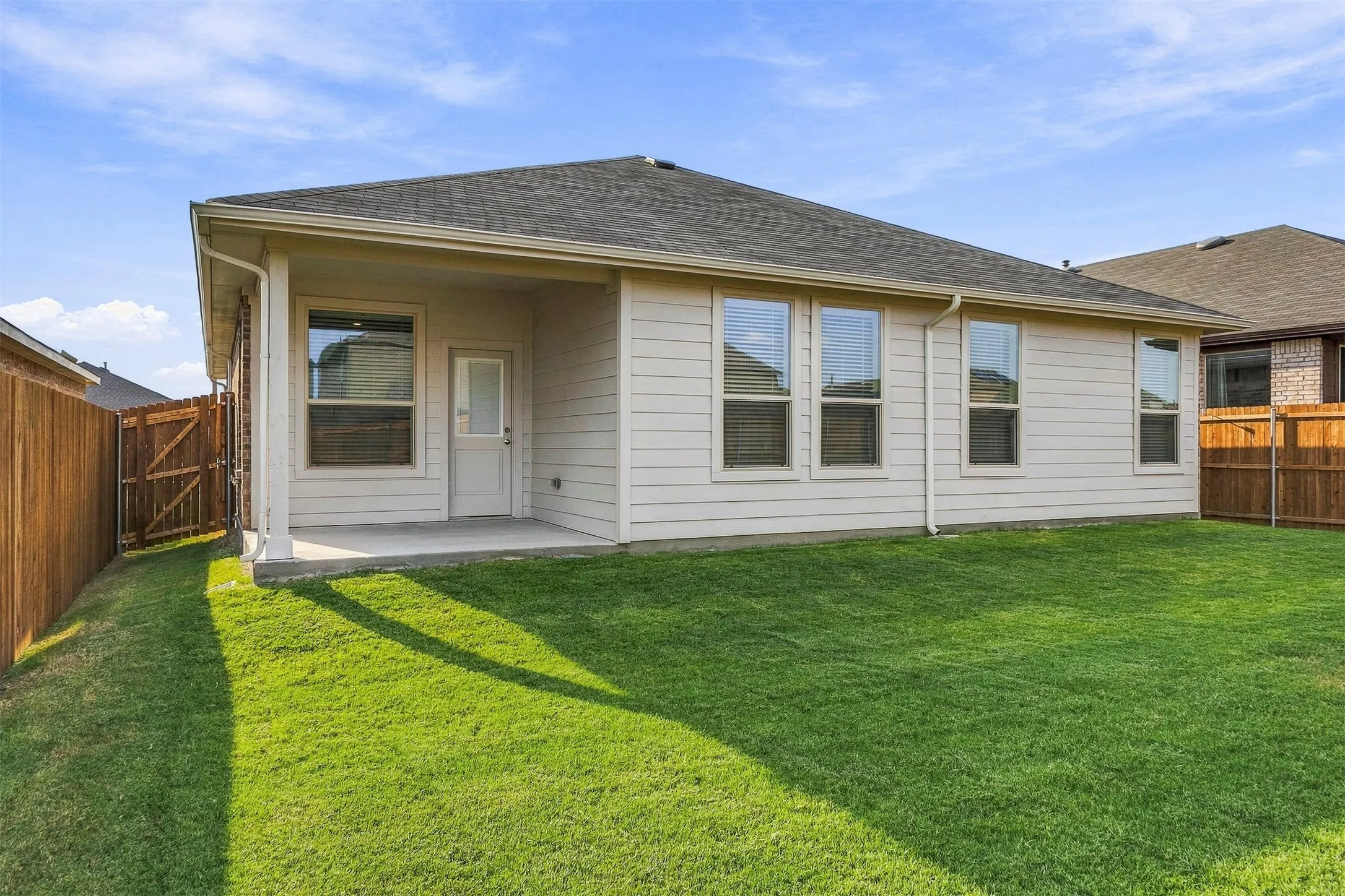 Expansive backyard featuring a manicured lawn, wood fencing, covered patio, and multiple windows