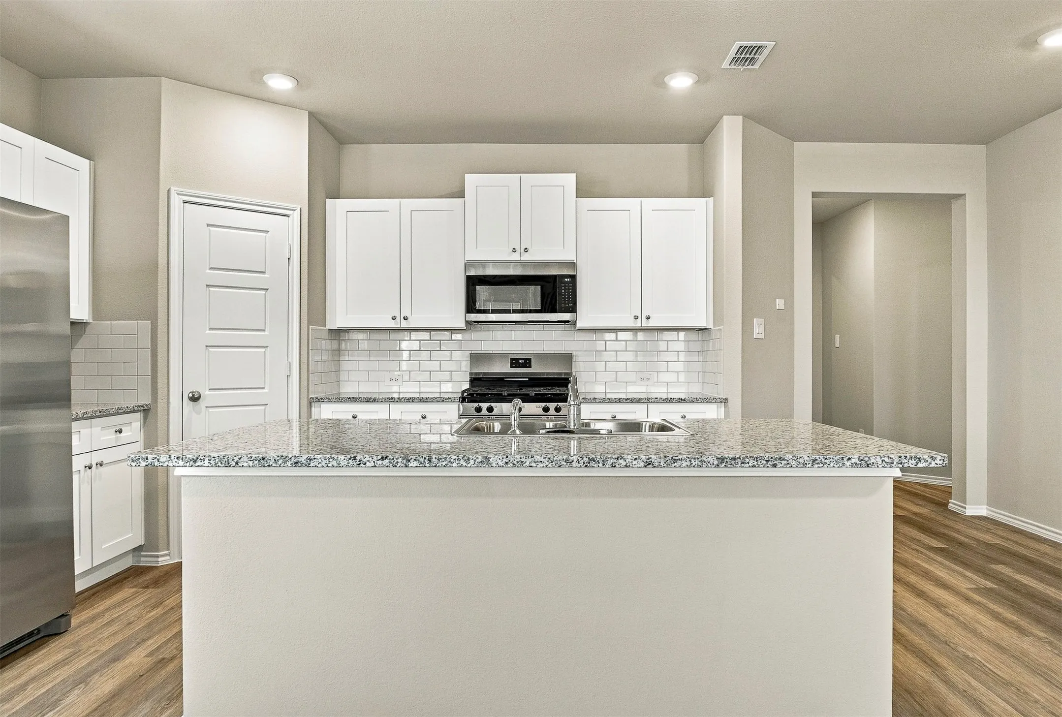 Kitchen featuring white cabinetry, subway tile backsplash, stainless steel appliances, wood-finish flooring, and a breakfast bar with stone countertops